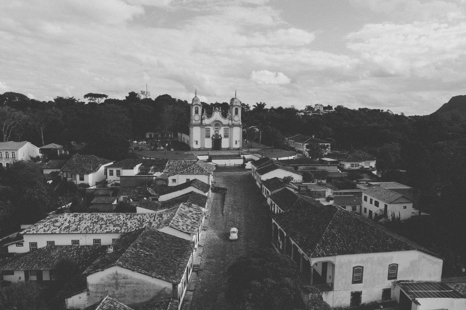 Historic black and white aerial view of a colonial Brazilian town with a prominent church and tiled rooftops in the hills.