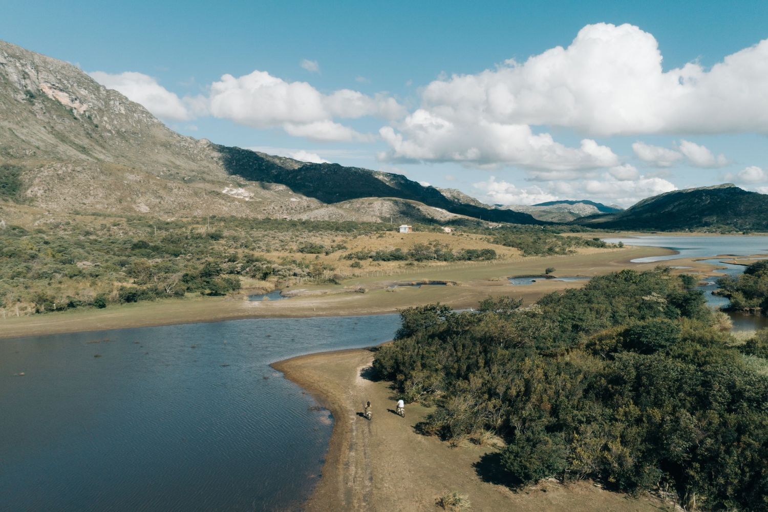 A winding river flows through mountainous terrain with brush-covered banks under a partly cloudy sky.