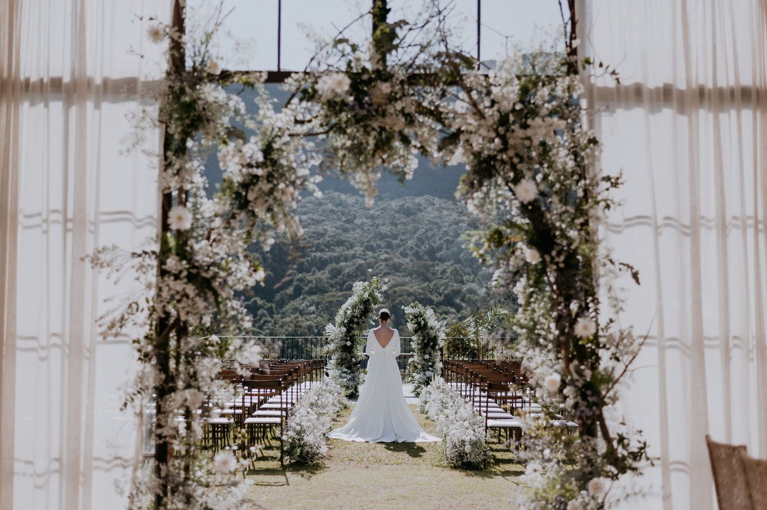 Wedding ceremony floral arch with white flowers and greenery framing a mountain vista backdrop.