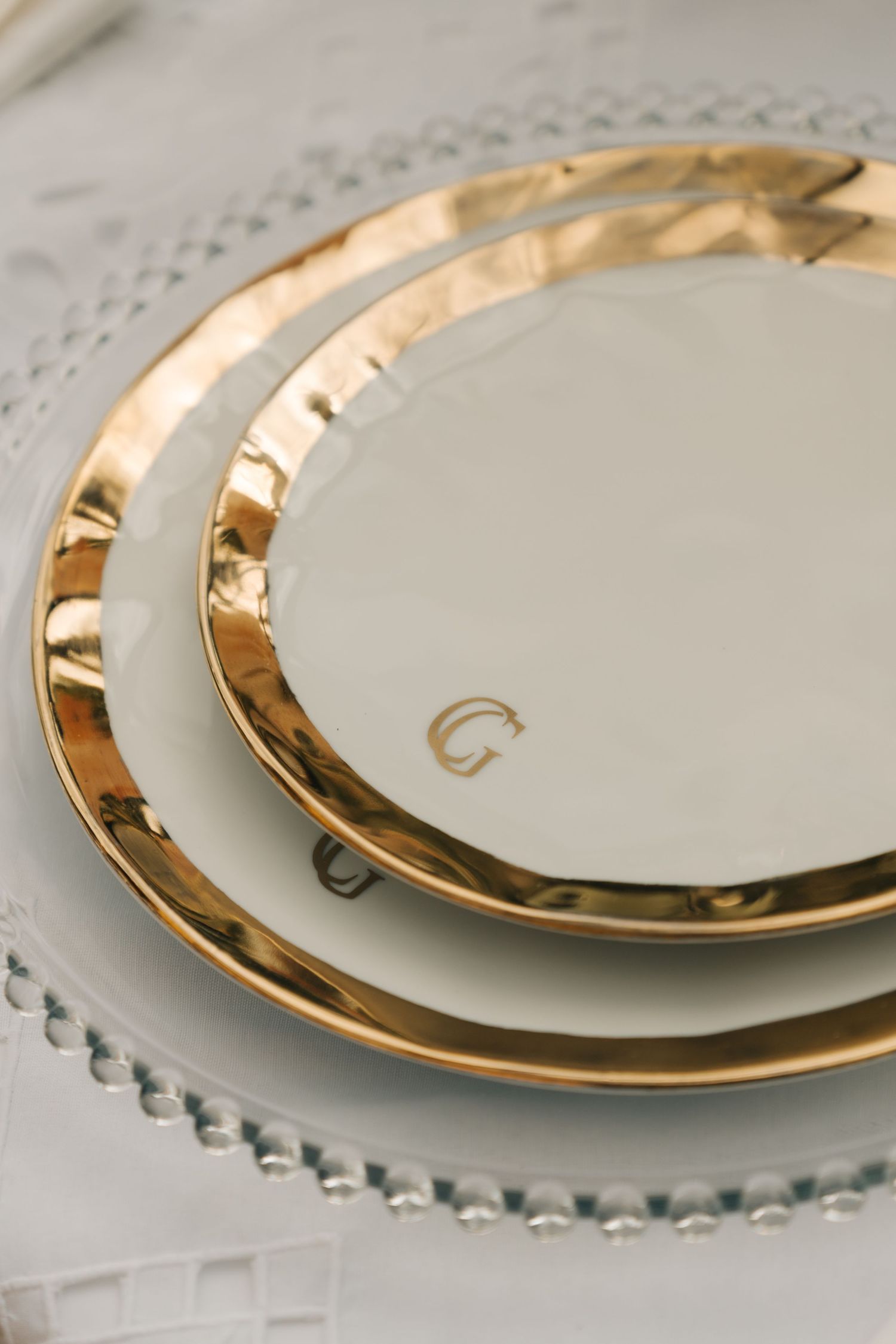 White and gold rimmed fine china plates stacked on delicate lace tablecloth.