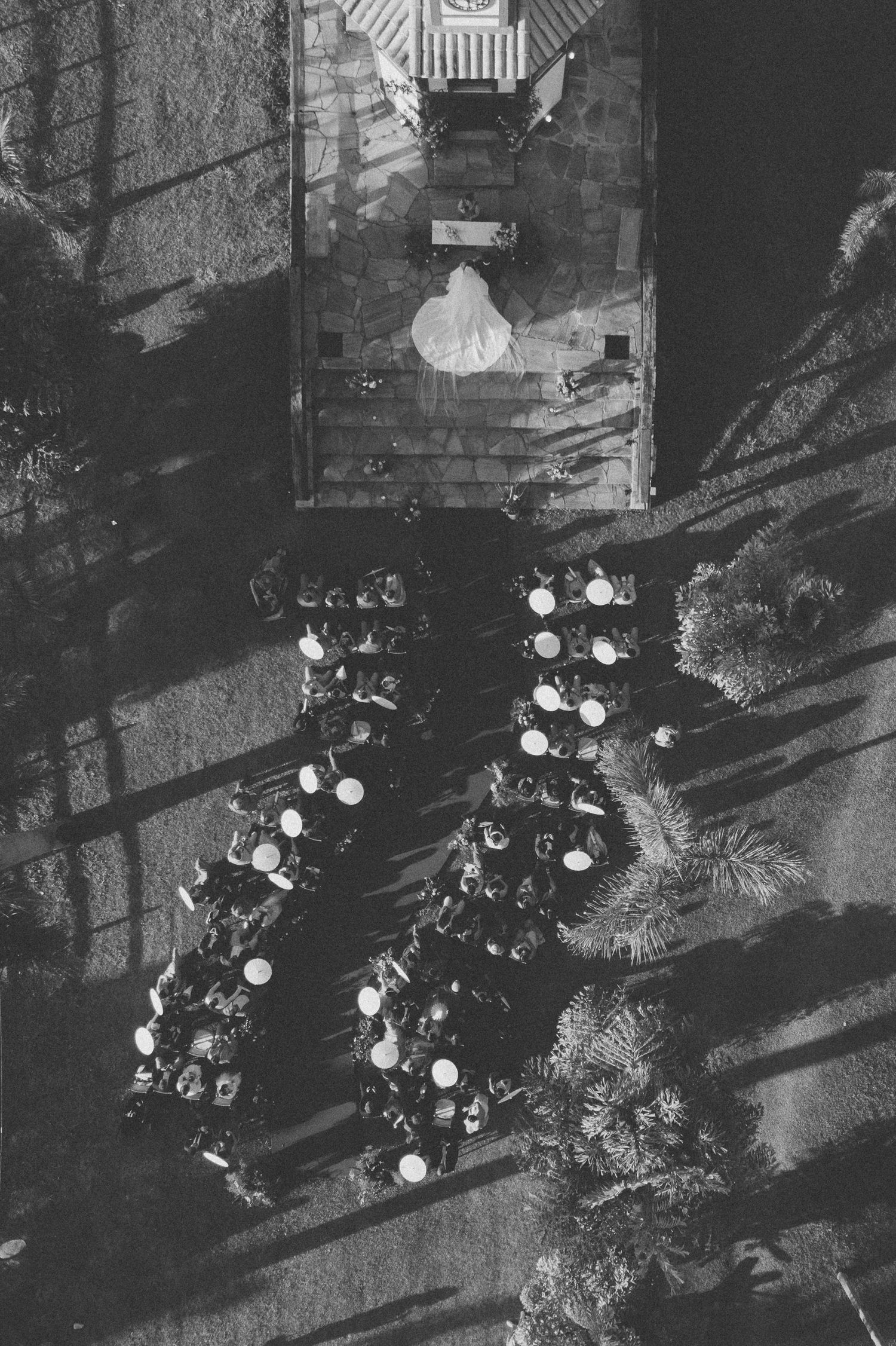 Aerial black and white view of an outdoor wedding reception setup with round tables and string lights.