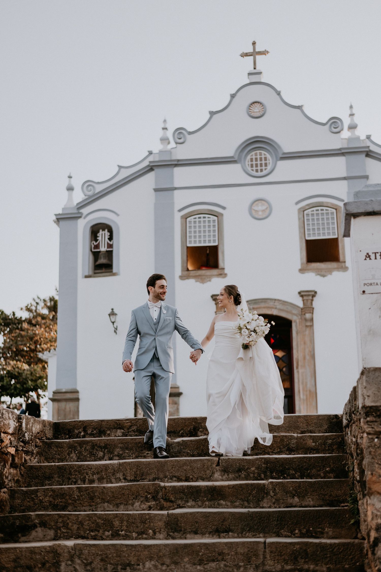 Couple descending white church steps after traditional wedding ceremony.