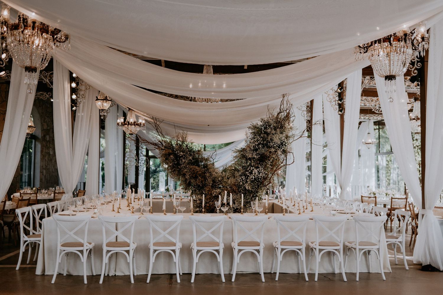 Modern wedding reception space with white draping and greenery centerpieces.