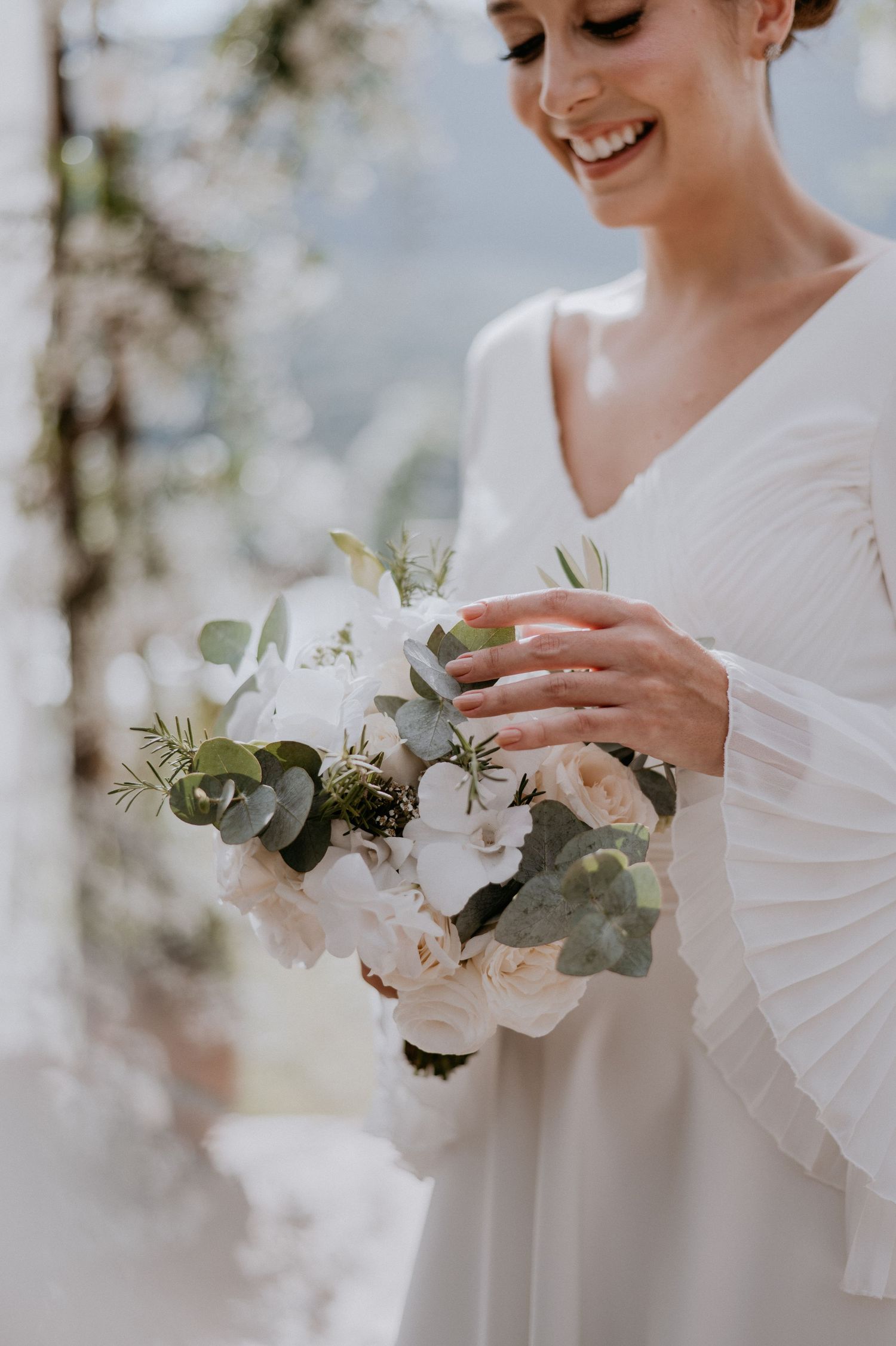 Bride holding a beautiful white and green bouquet while smiling.
