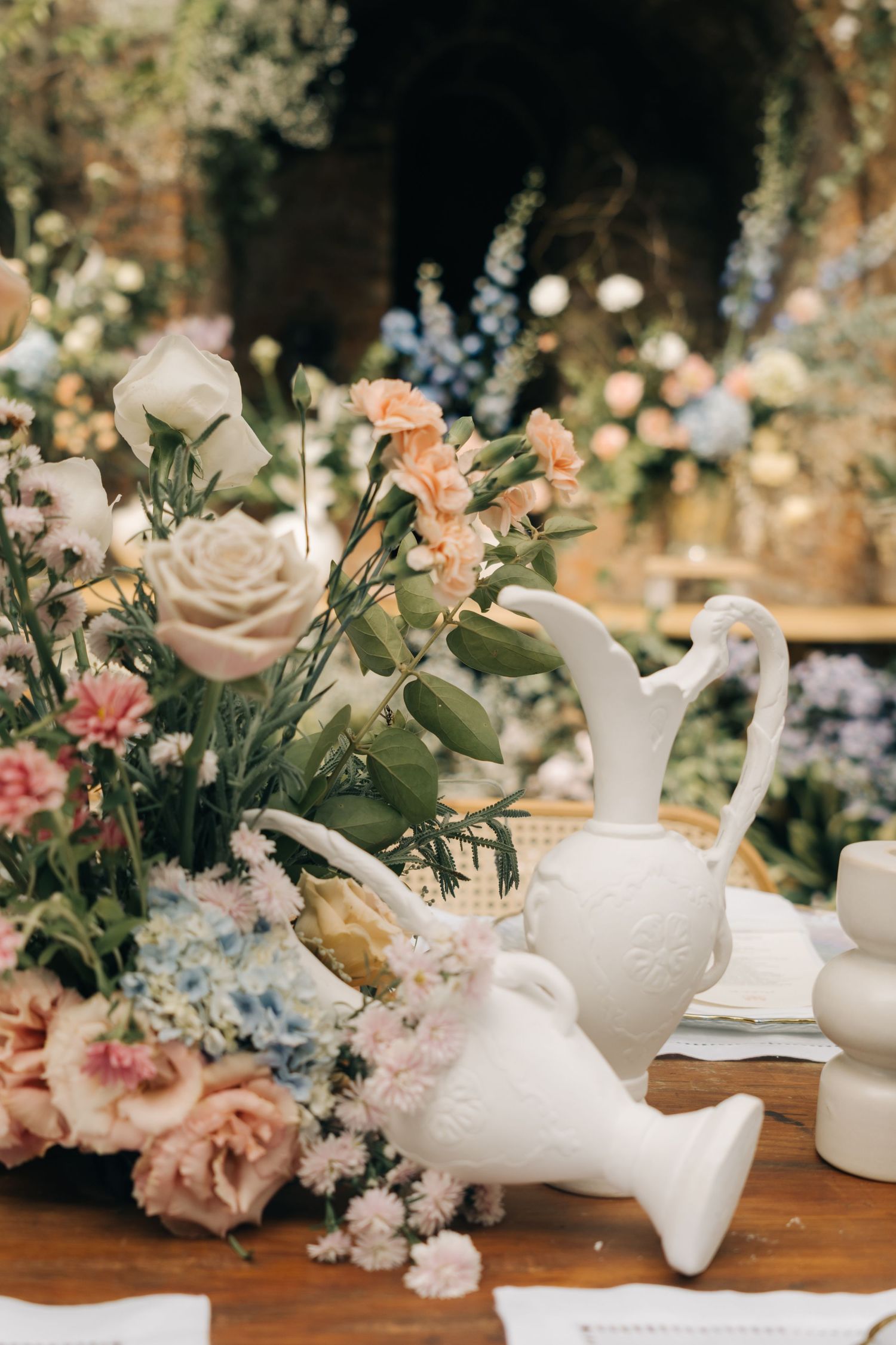 Vintage white ceramic pitchers with soft pink roses and delicate floral arrangements on wooden table.