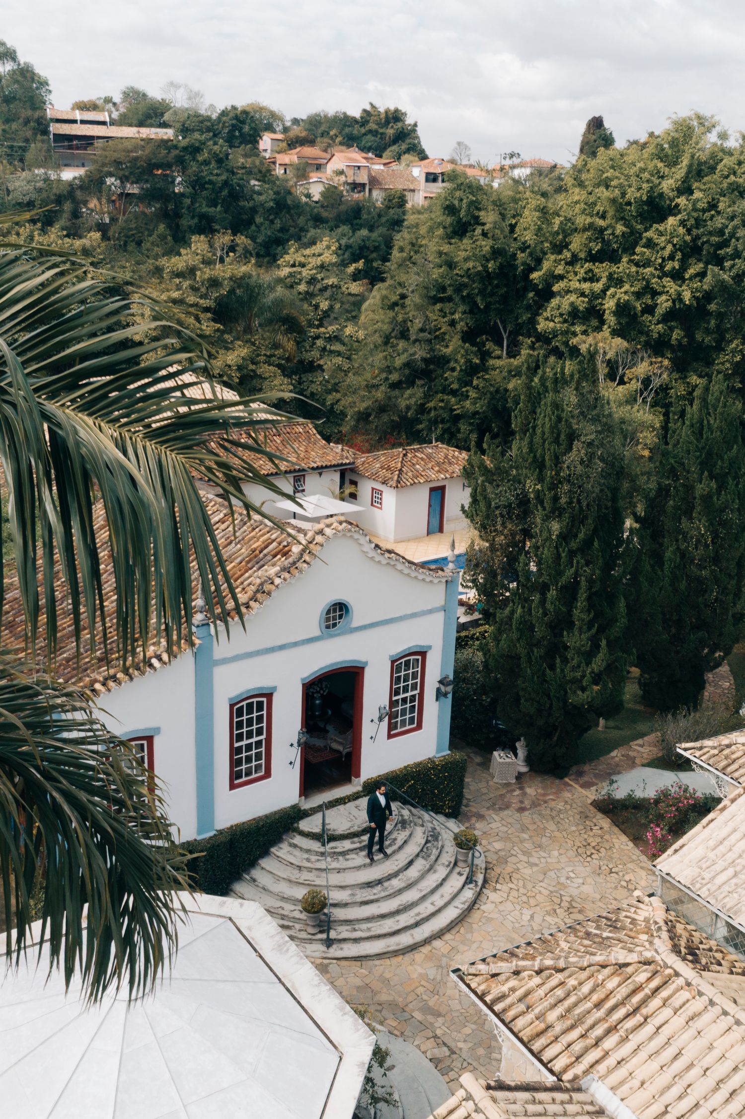 White colonial church with blue trim nestled among palm trees and terracotta roofs on a hillside.