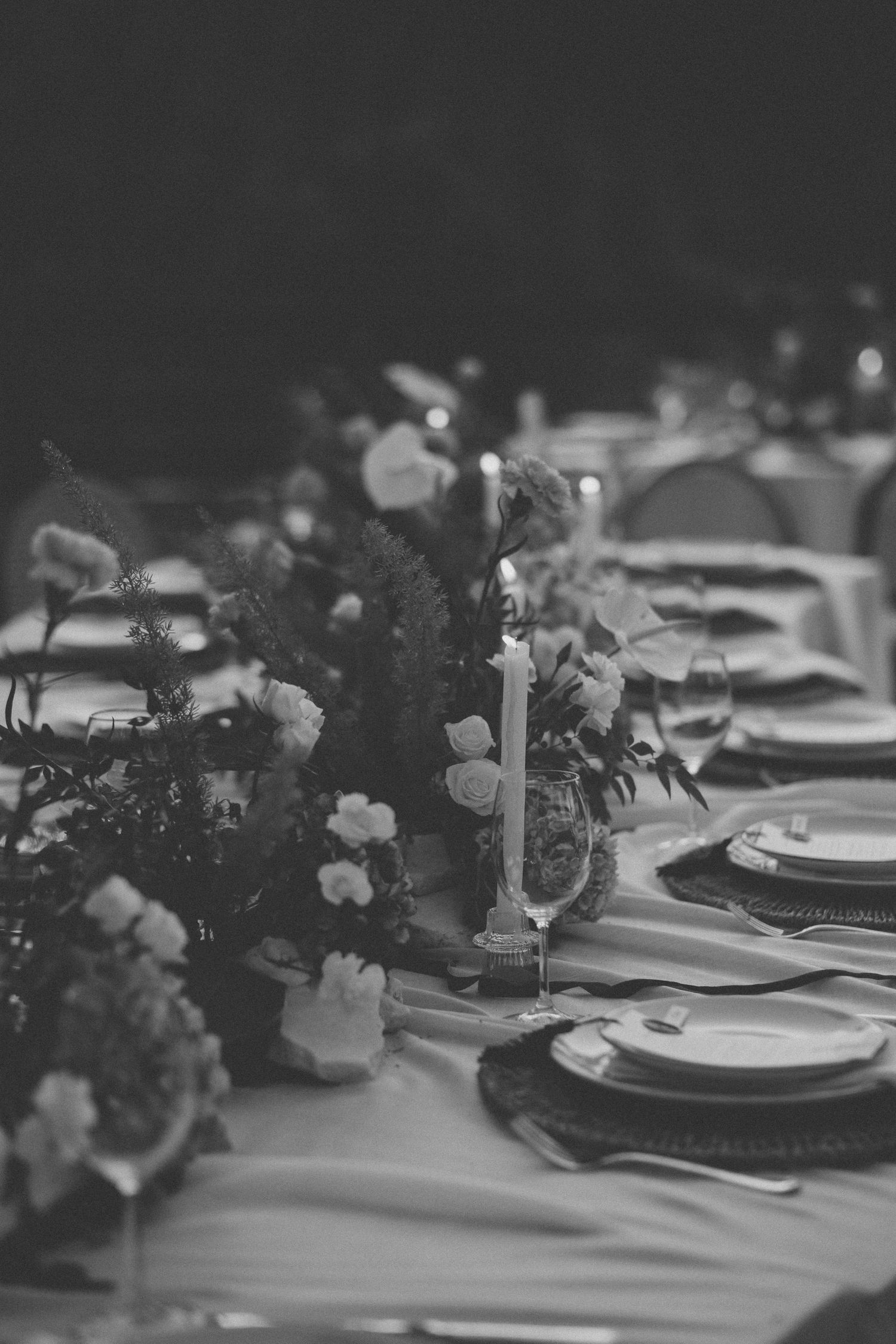 Black and white elegant table setting with floral centerpieces and place settings arranged in a row.