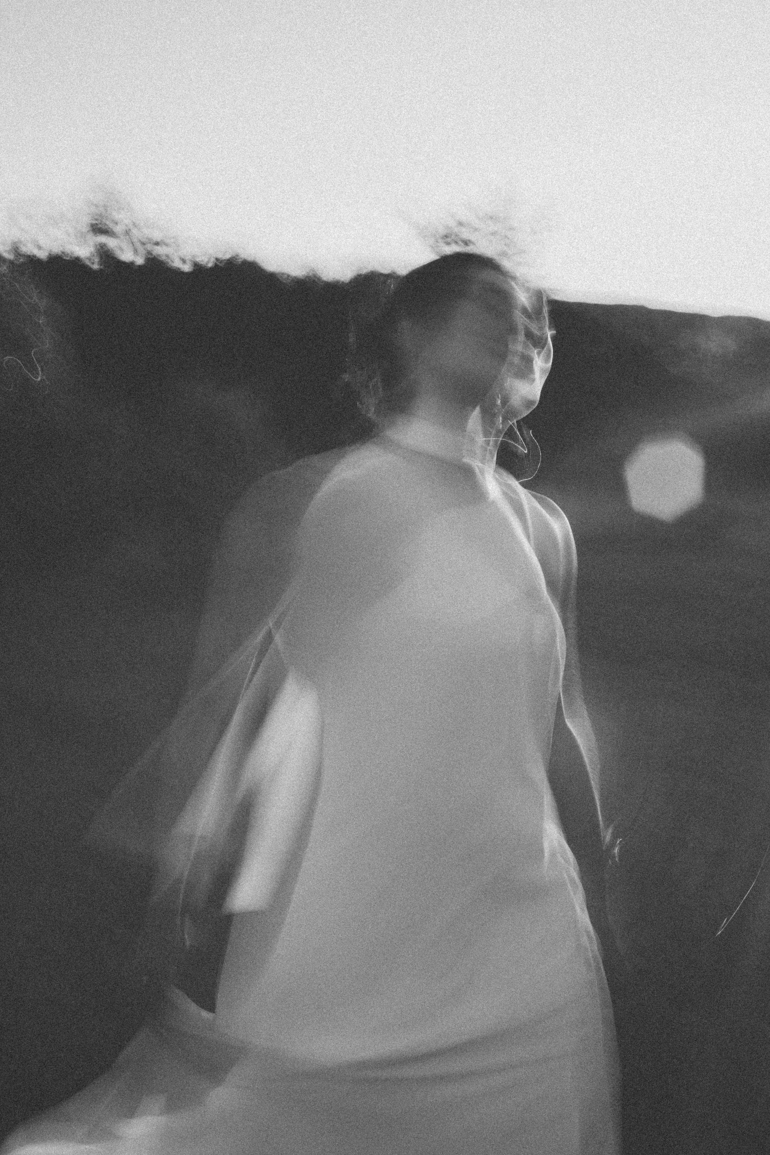 Dreamy black and white artistic photograph showing blurry motion of person in flowing white dress against dark background.