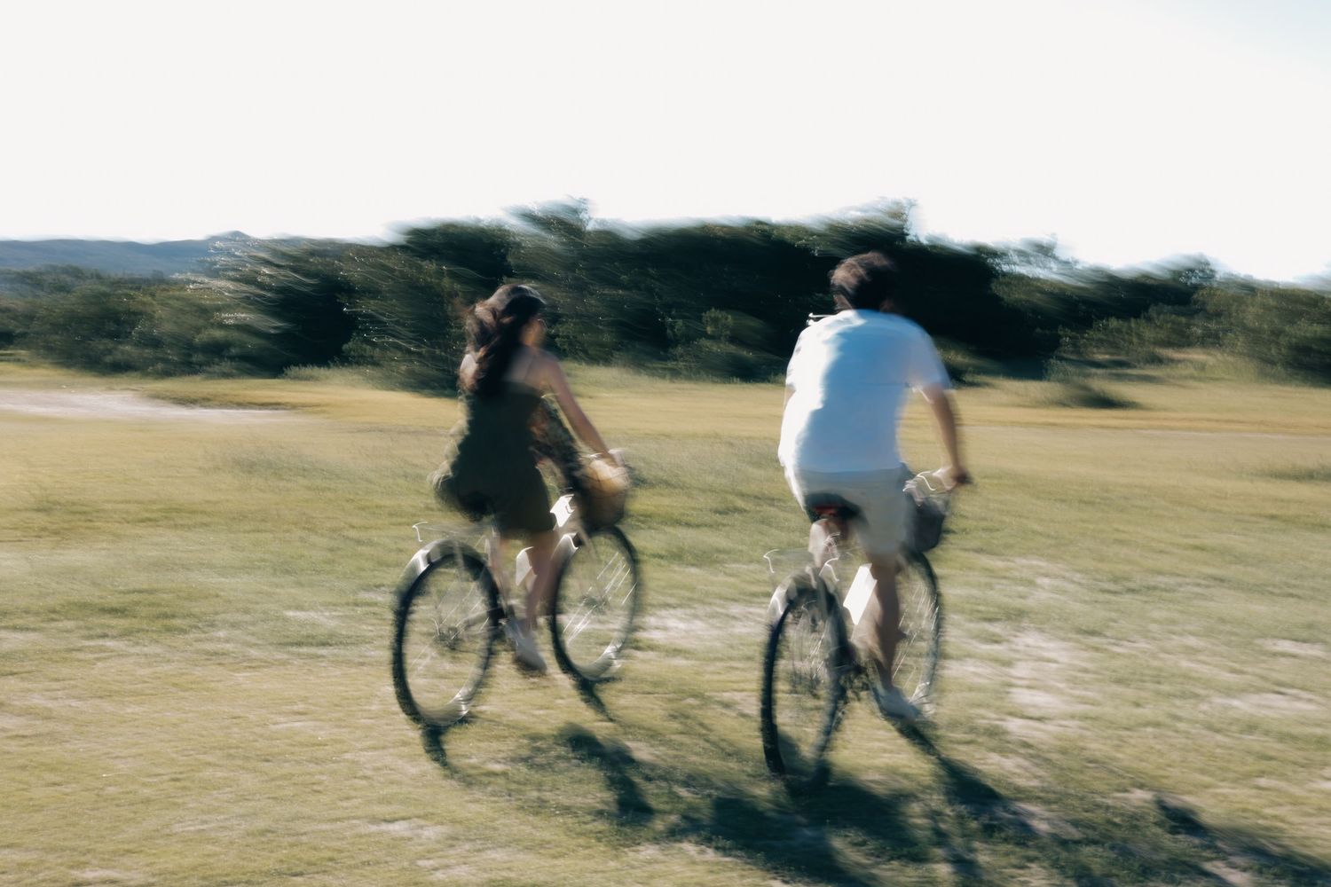 A sequence of motion shots showing cyclists riding bikes across a grassy hillside on a sunny day.