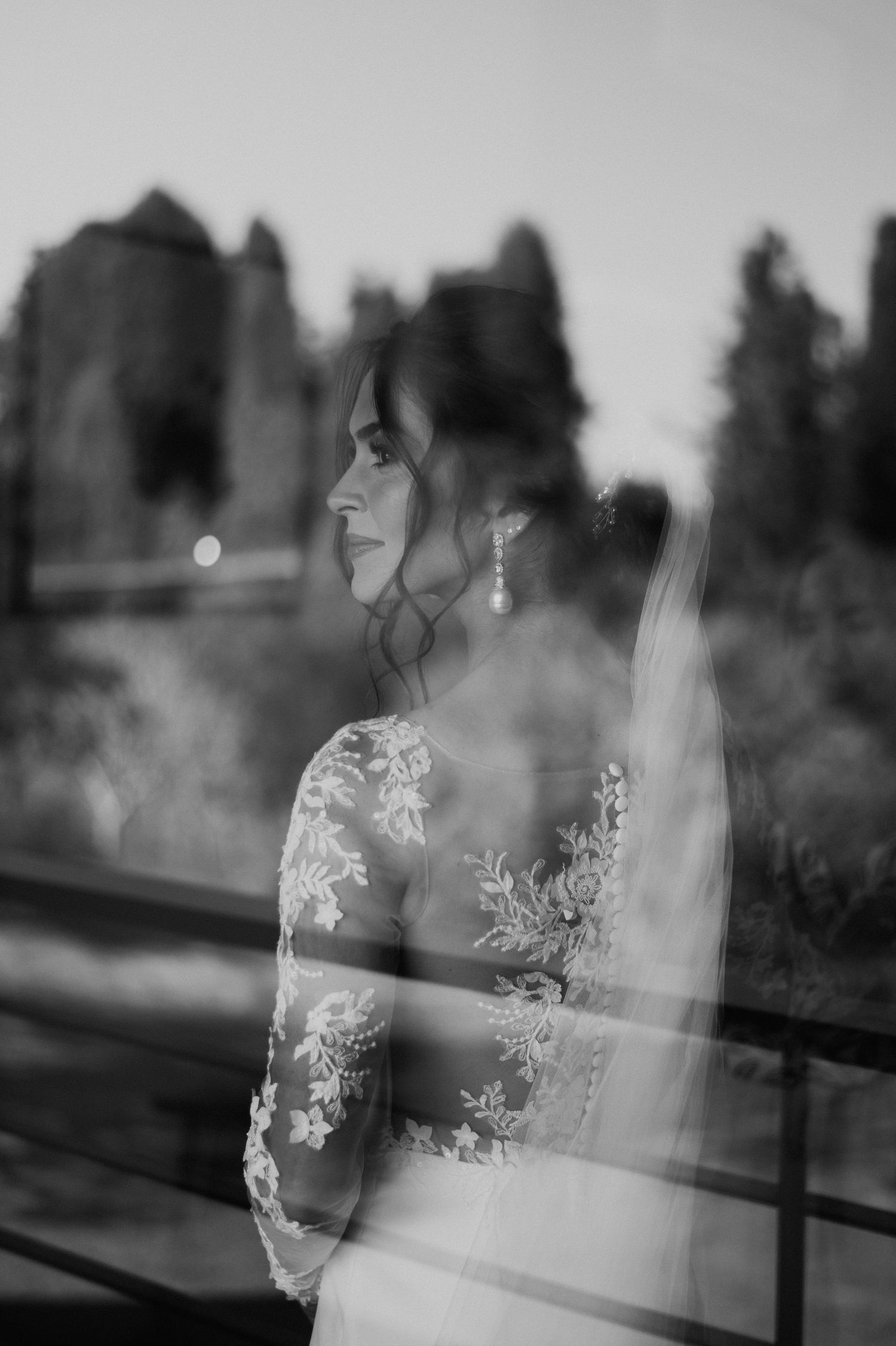Artistic black and white double exposure bridal portrait with lace details through window reflection.