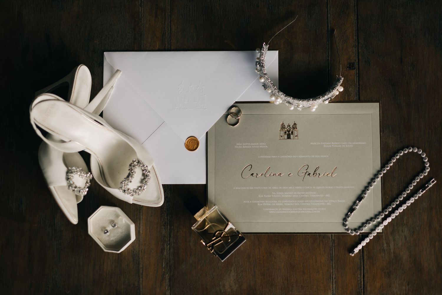 Wedding accessories including white heels, jewelry, and a formal invitation laid on a dark wooden surface.