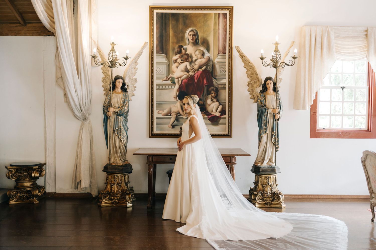 Classic white wedding dress with long train shown in an elegant church interior with religious artwork and statues.