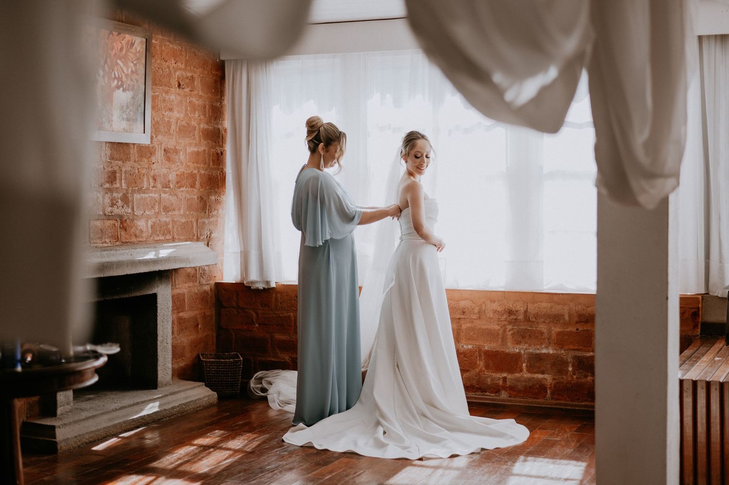 Two figures in a sunlit room preparing wedding attire with exposed brick walls.