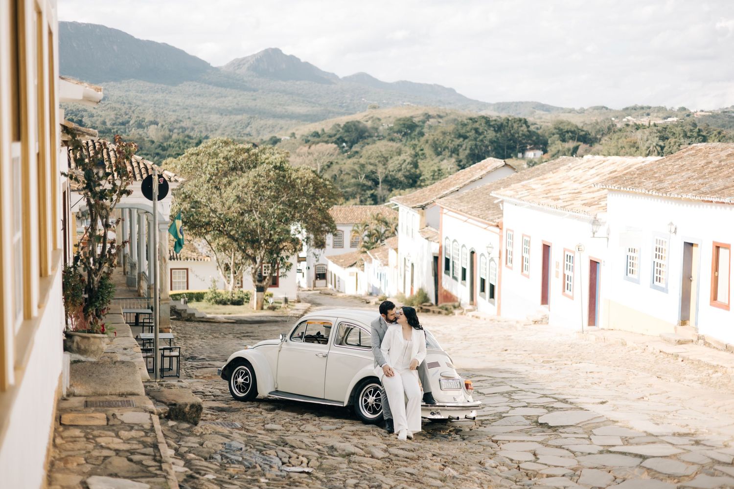 Vintage Volkswagen Beetle parked on cobblestone street in a colonial town surrounded by mountains.