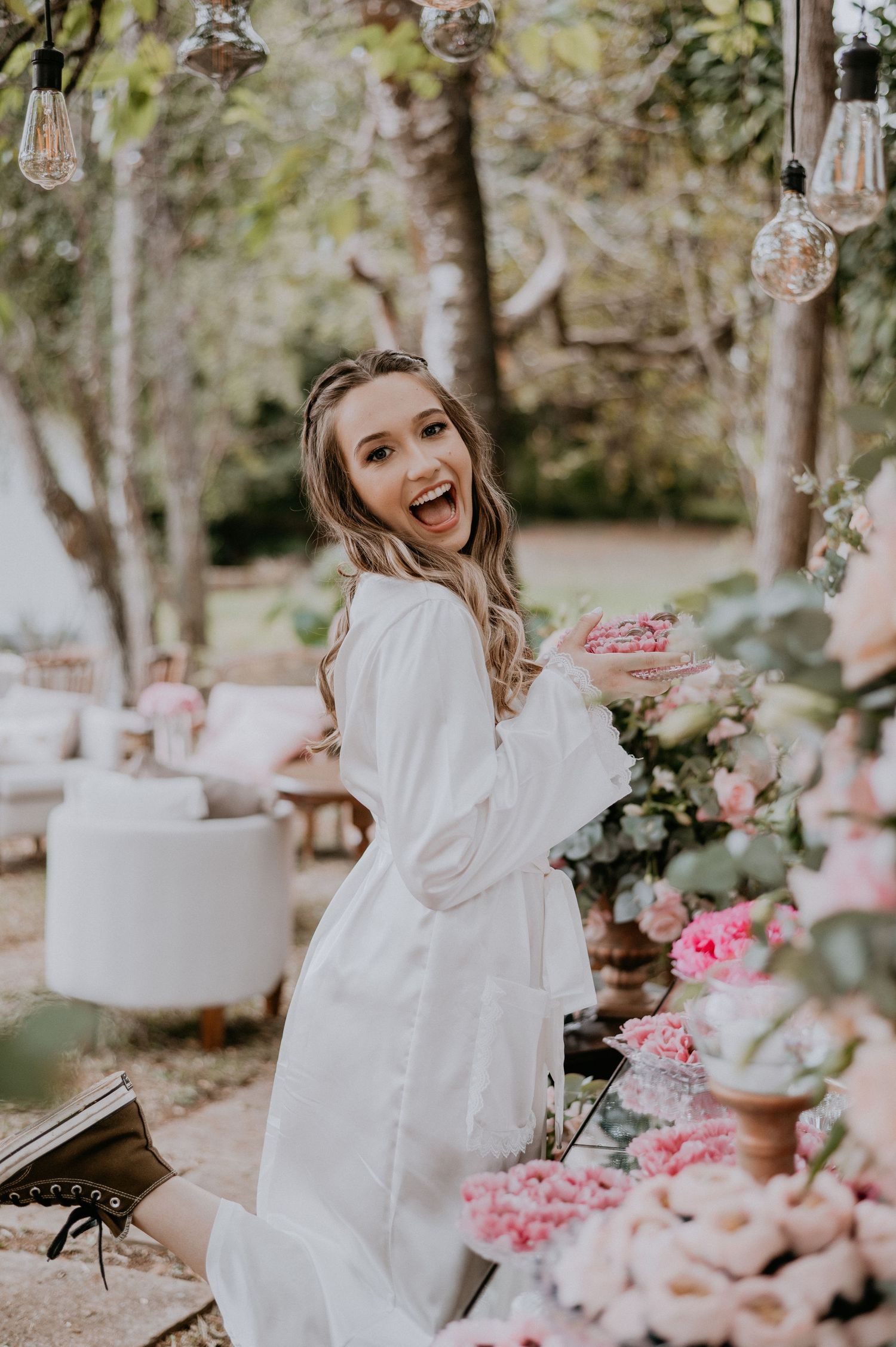 Candid bridal getting ready moment surrounded by floral decorations and string lights.