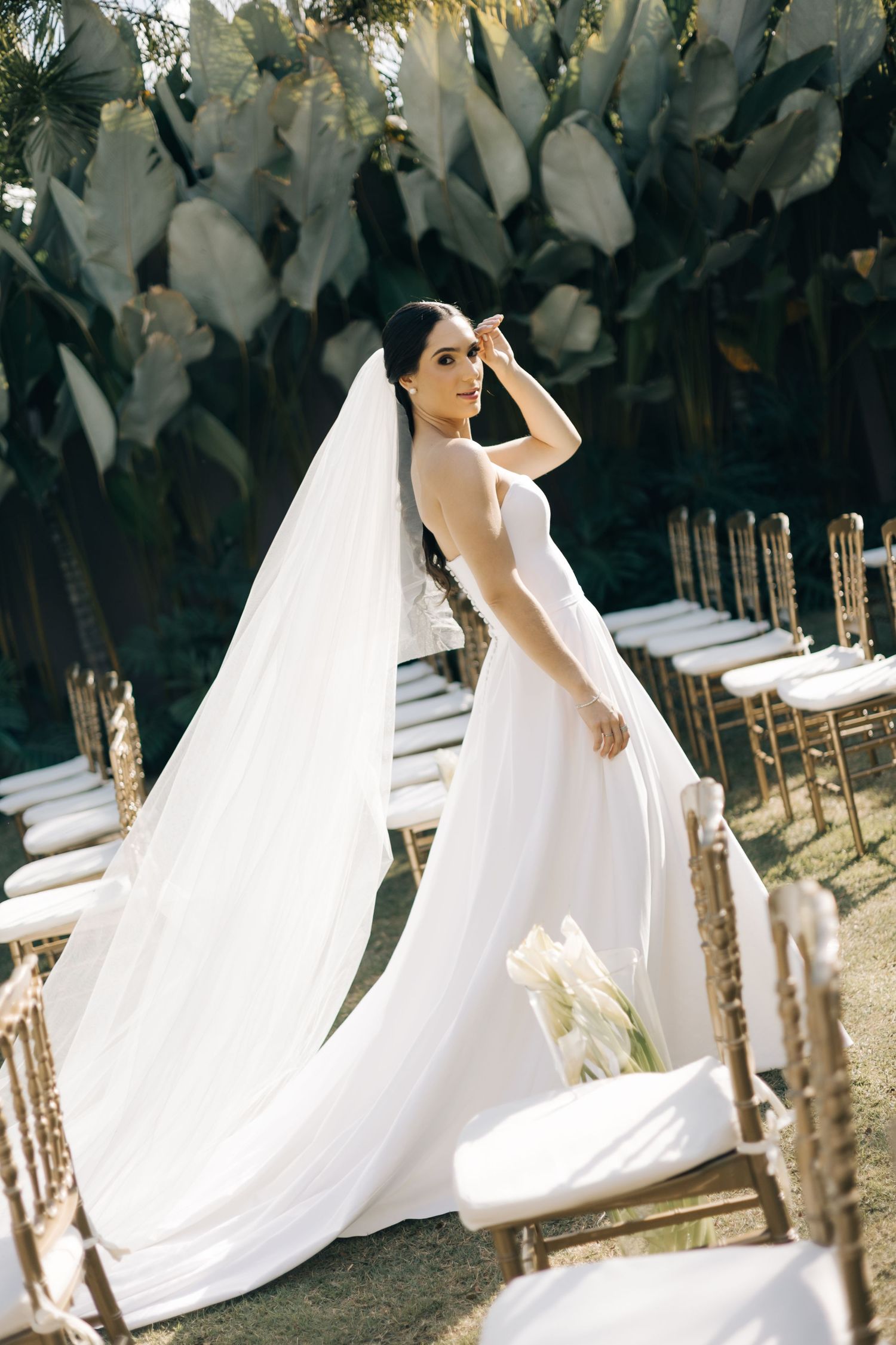 A stunning wedding dress with a flowing long veil captured in an outdoor garden setting with decorative chairs.