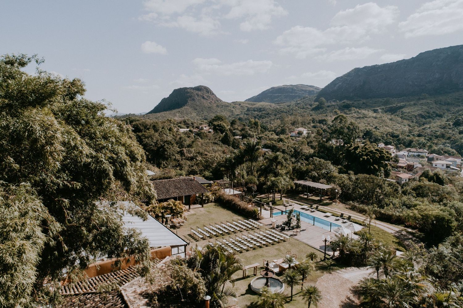 Aerial view of an outdoor venue with mountain scenery and swimming pool in a lush tropical setting.