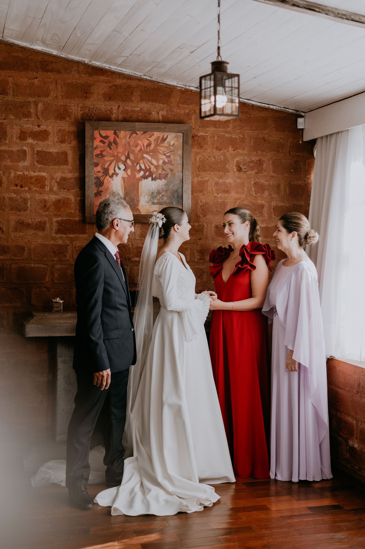 Wedding party gathering in a rustic brick room with elegant dresses and formal attire.