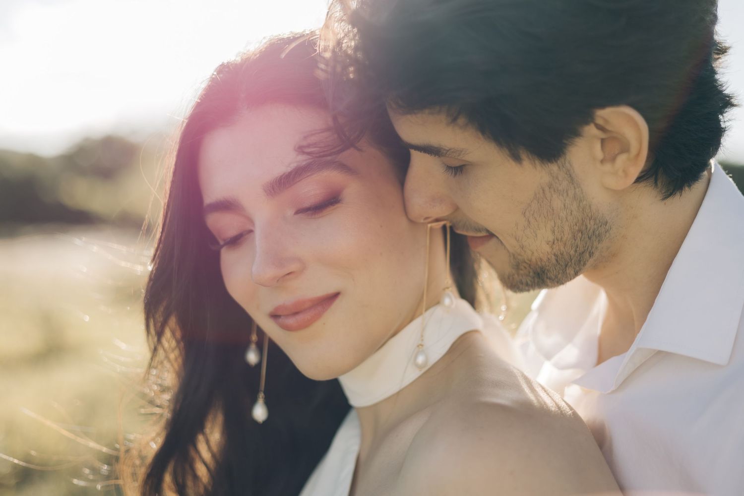 Close up romantic couple in white clothes embracing in golden sunlight outdoors.