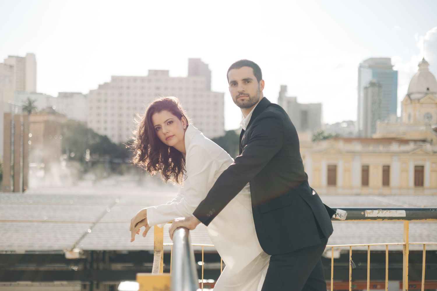 Couple in formal attire dancing together on urban rooftop with city skyline in background during sunset.