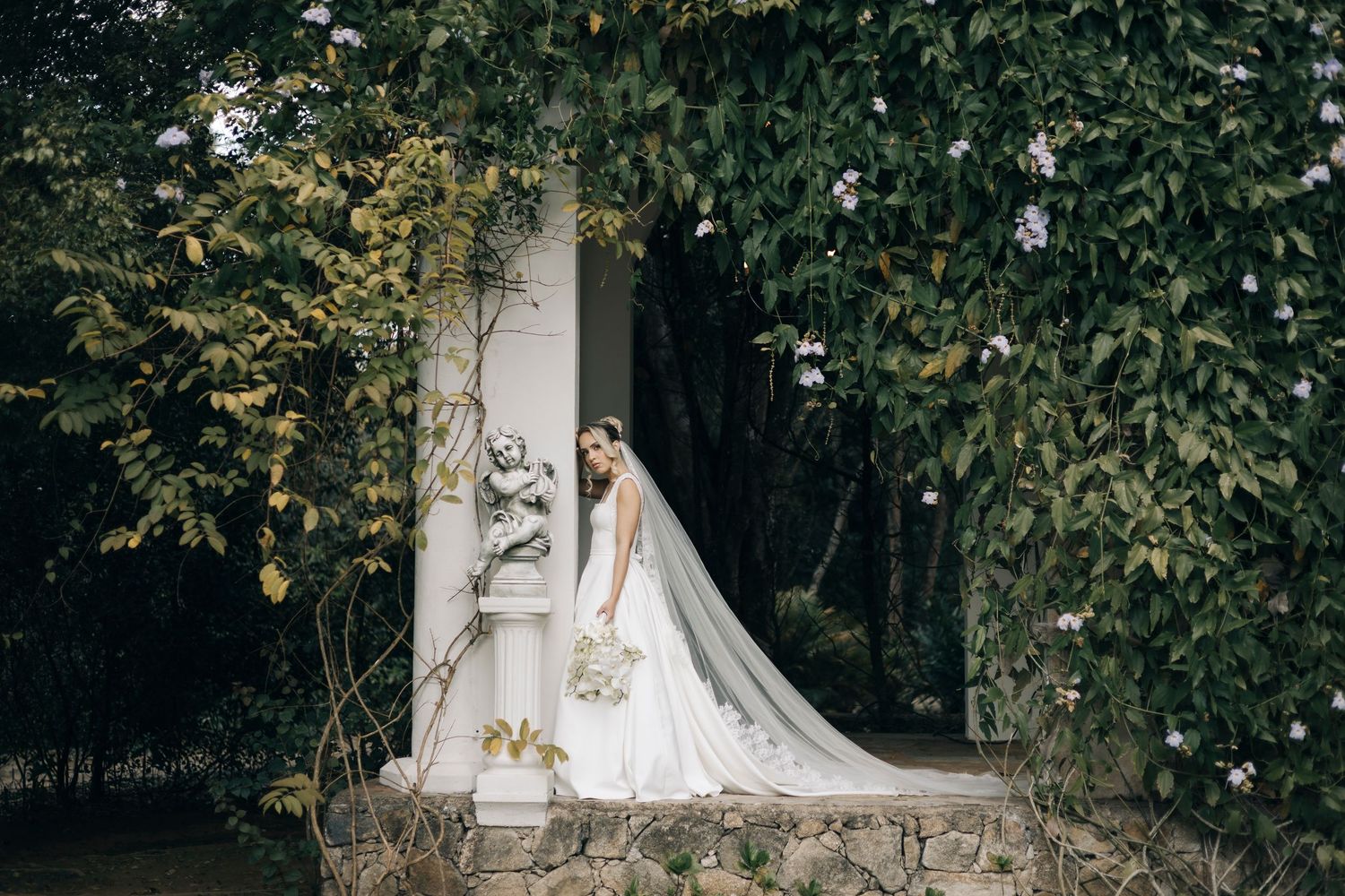 A series of romantic wedding photos showing a bride in a white gown posing elegantly among lush garden greenery.