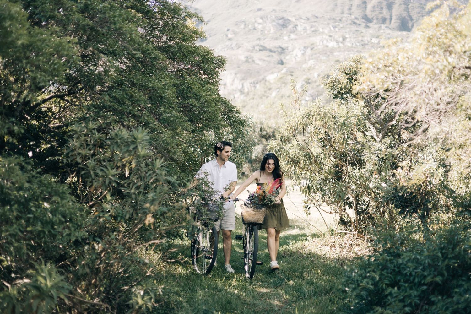 Two people enjoy a sunny hike together on a mountain trail surrounded by lush greenery and scenic views.