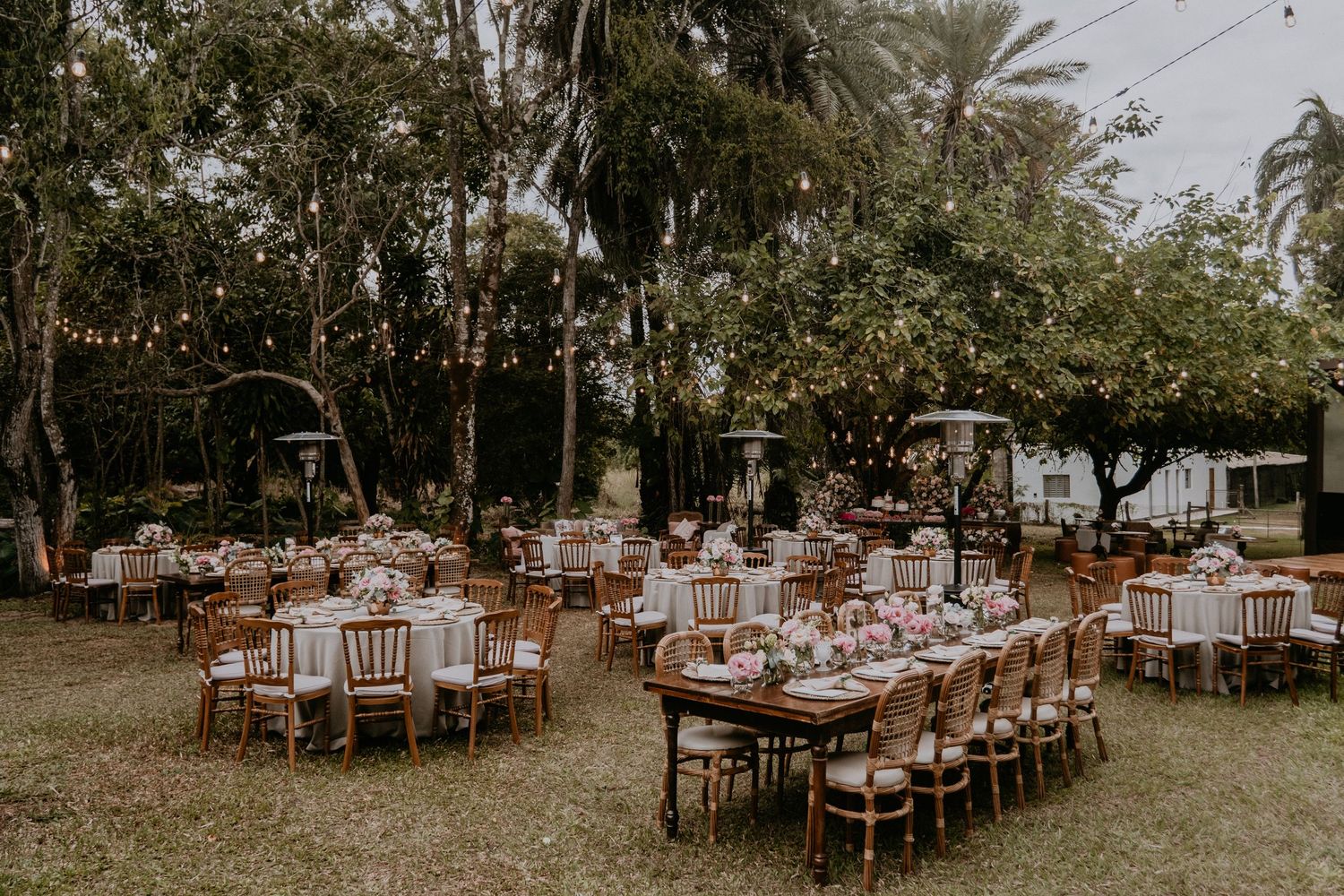 Garden wedding reception with round tables and wooden chairs arranged under string lights.