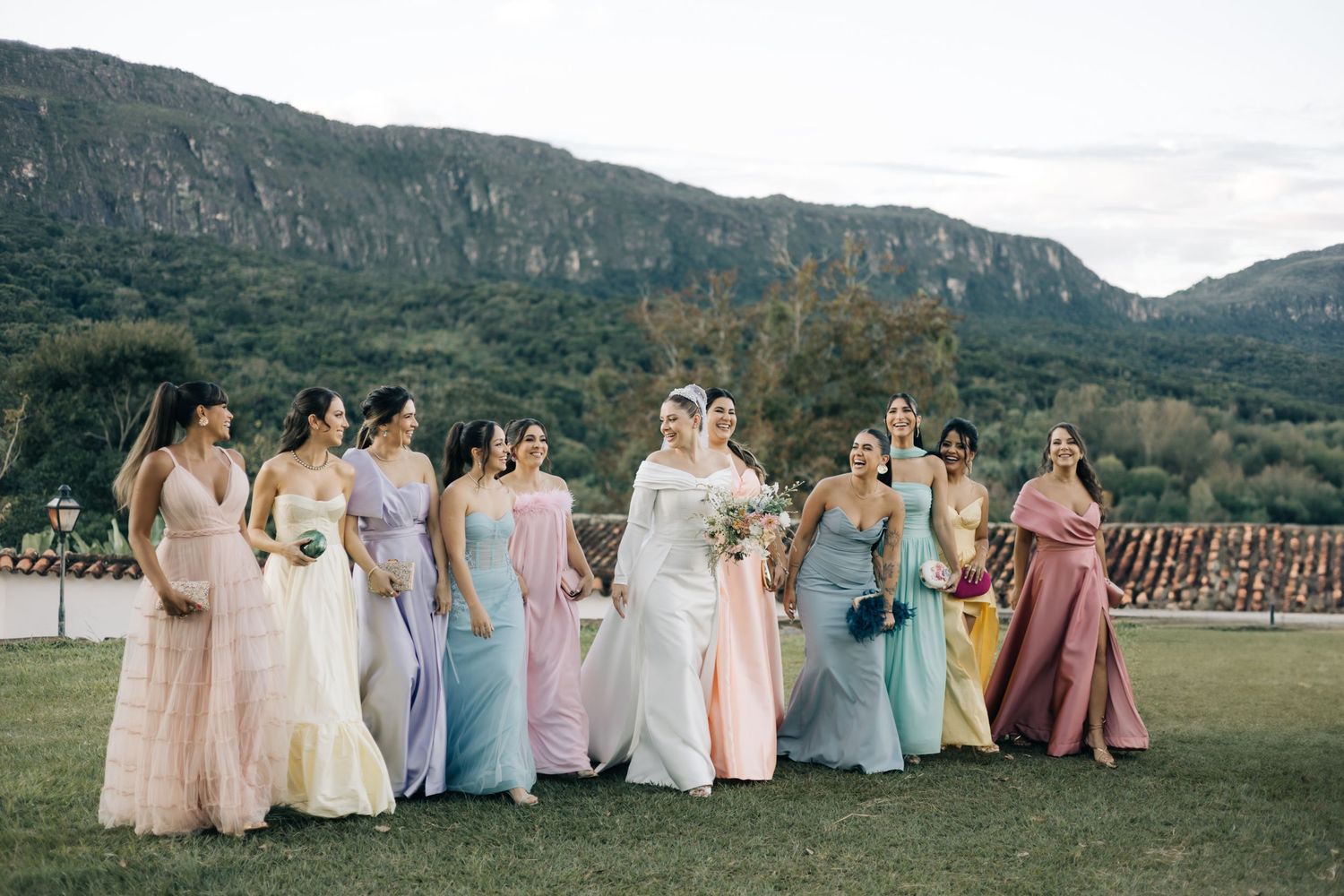 Bridal party in pastel dresses posing against mountainous landscape at sunset.