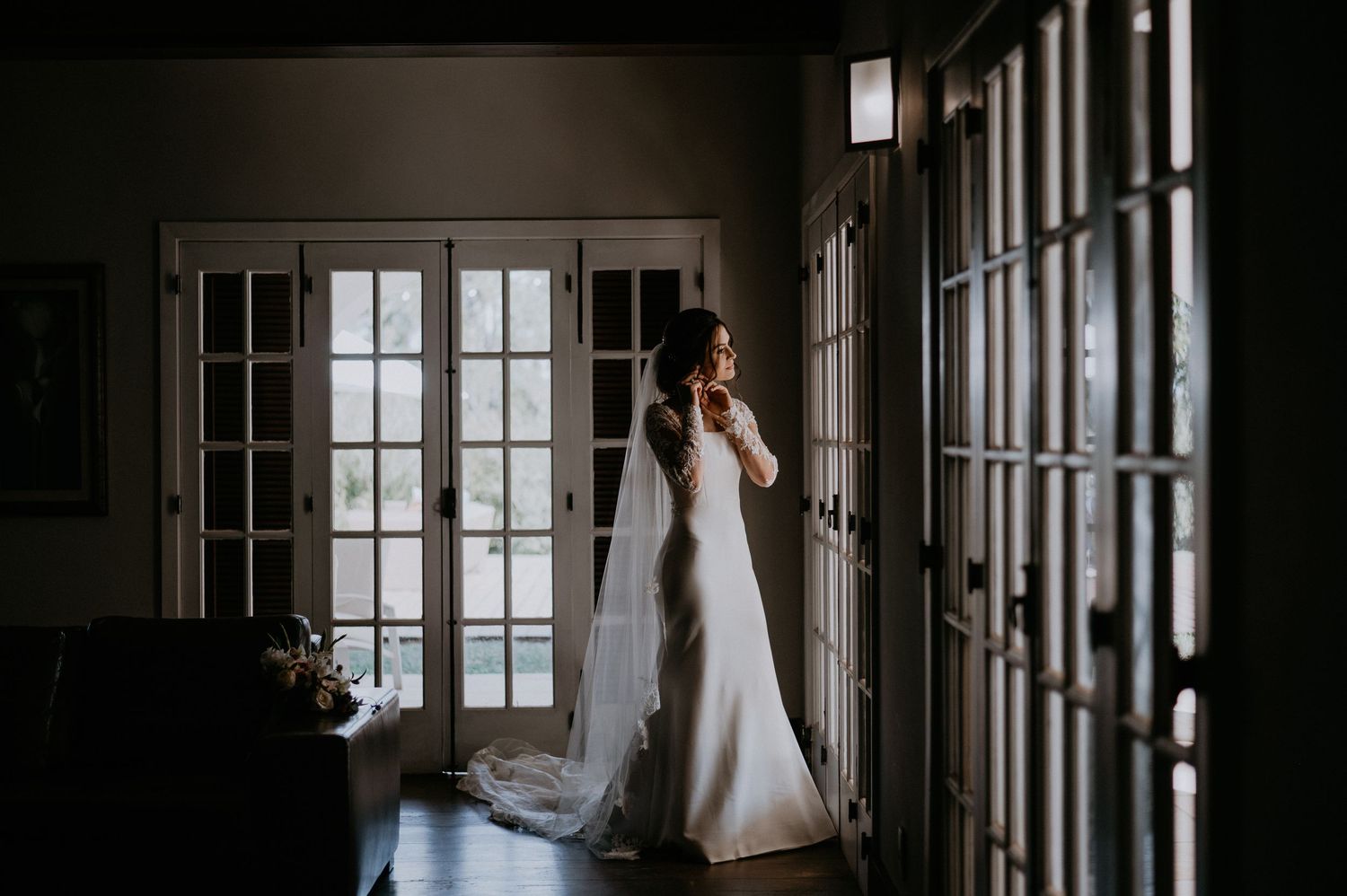 Moody silhouette of bride by French doors in elegant wedding gown.