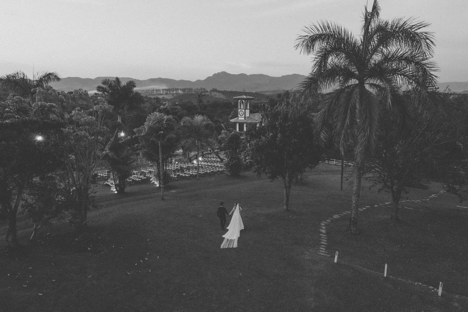 A black and white vintage photograph shows a figure in white walking across a palm tree-lined tropical landscape.