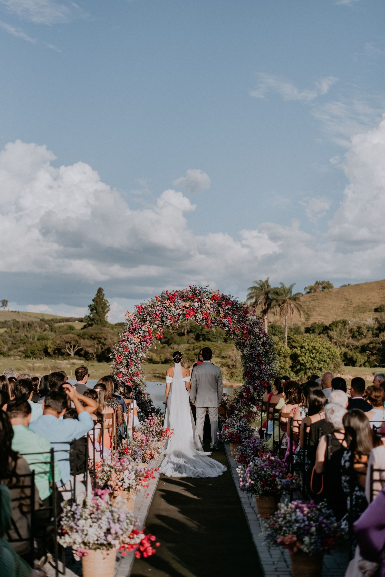 Outdoor wedding ceremony under floral arch with pink blooms against mountain backdrop.