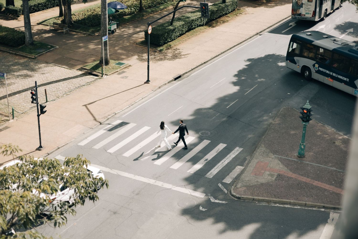 Aerial view of a person crossing a pedestrian crosswalk at an urban intersection on a sunny day.