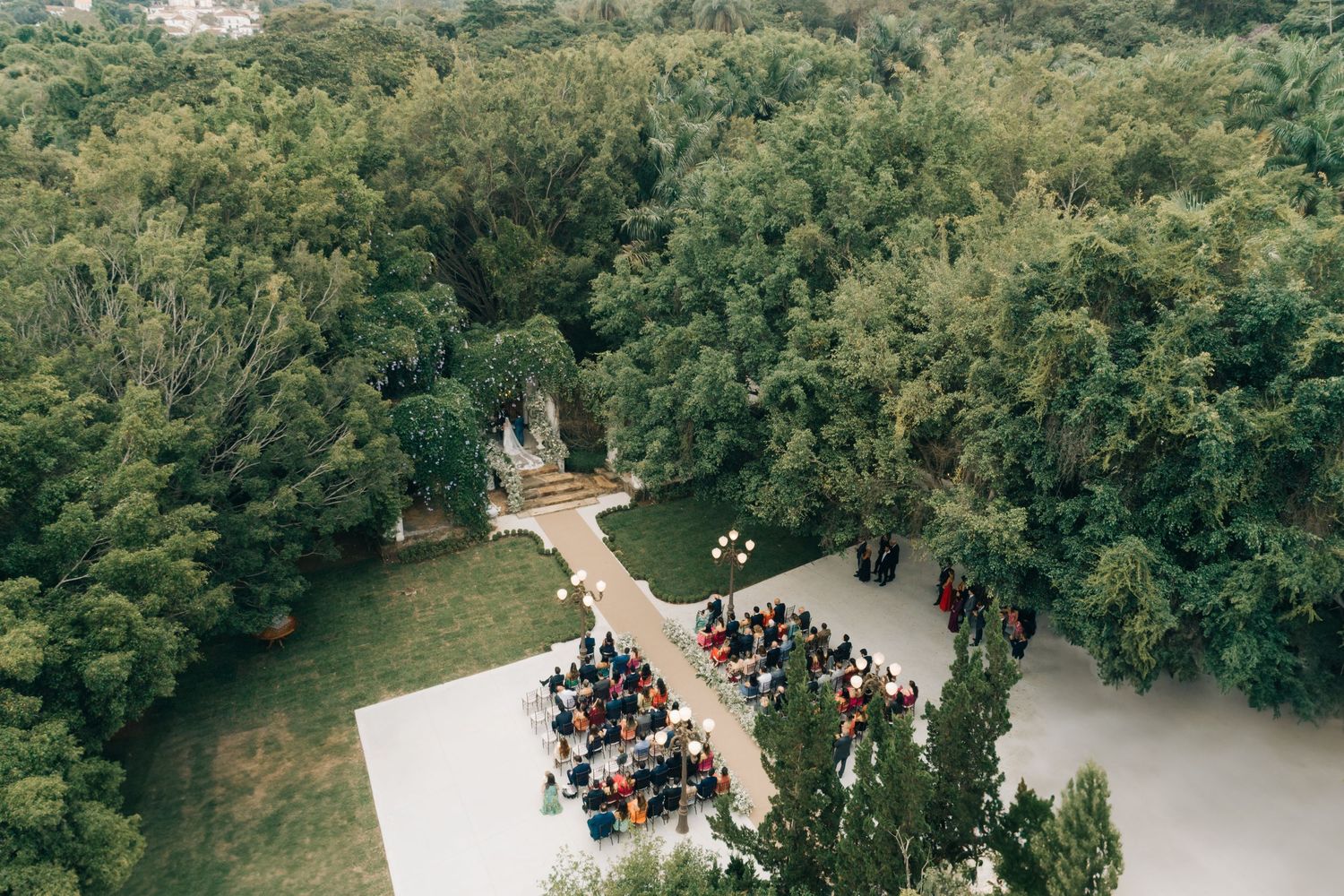 Aerial view of an outdoor wedding ceremony surrounded by lush green forest.