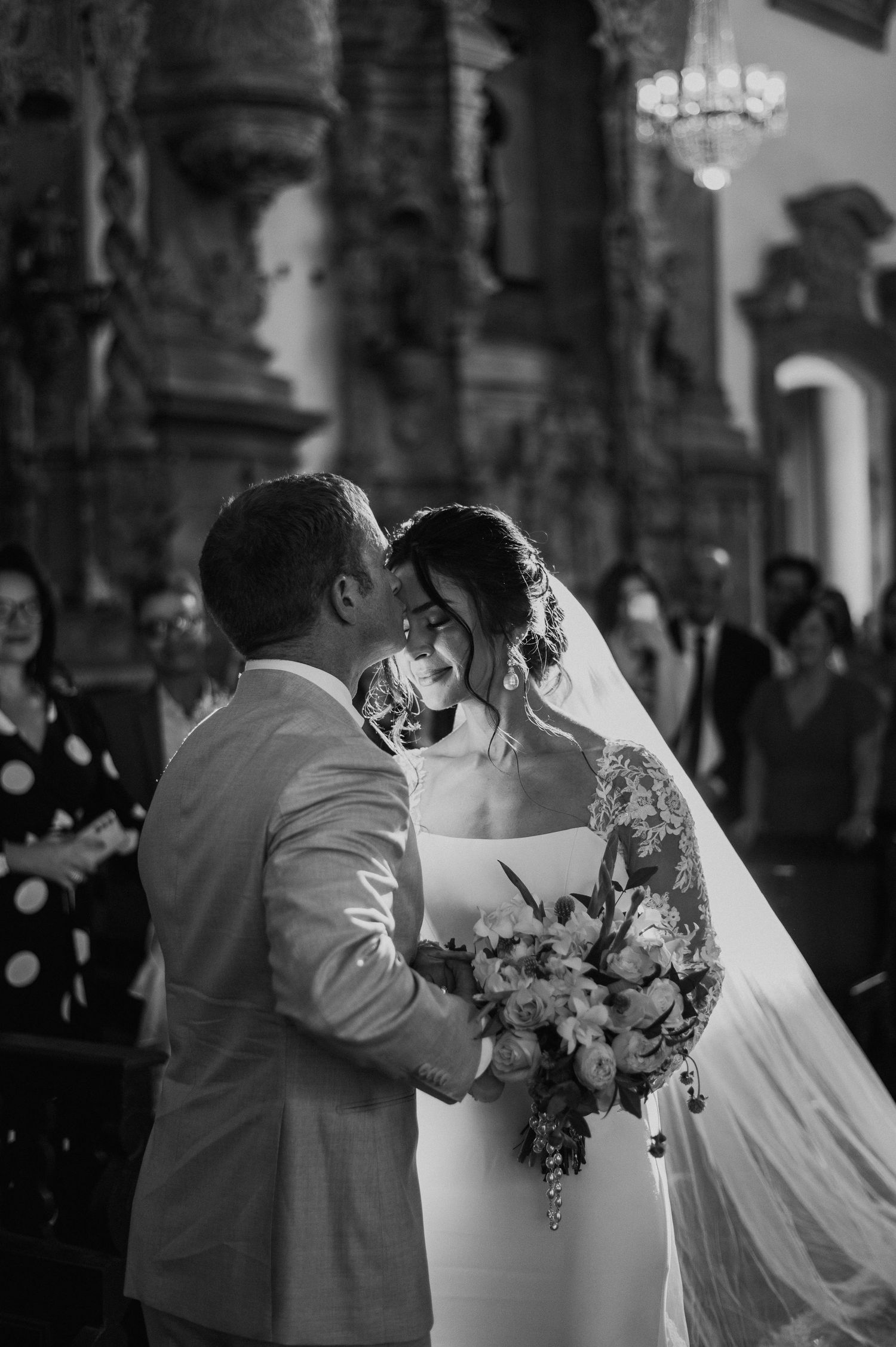 Romantic moment during church ceremony with elegant decor and flowing bridal veil.