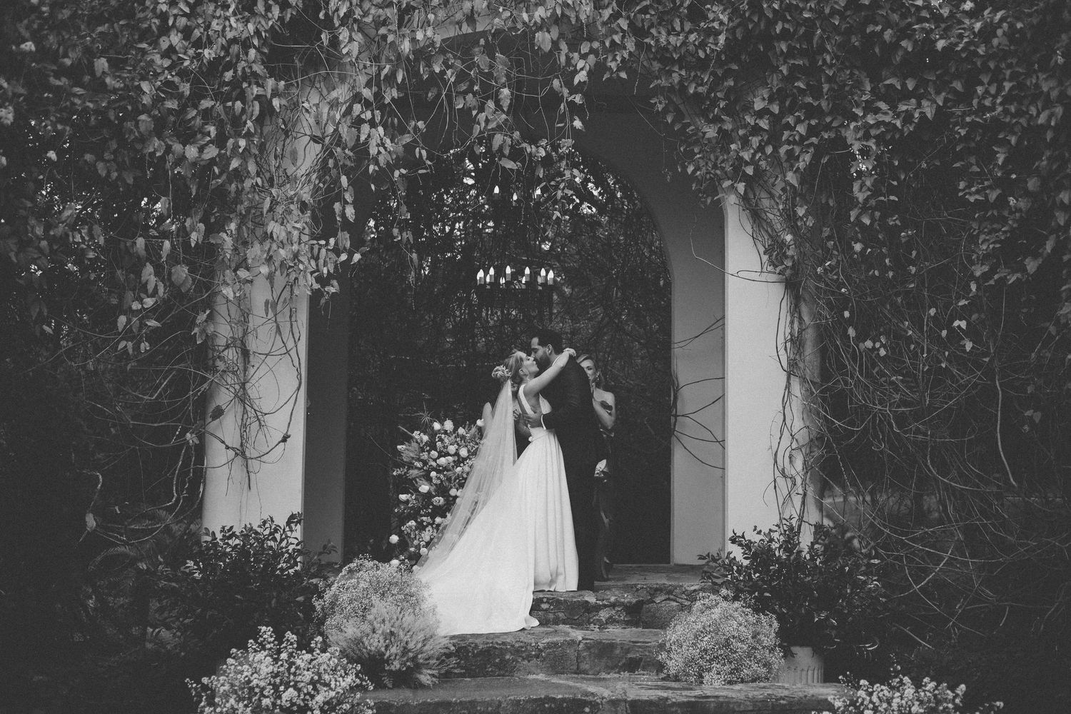 Romantic garden archway covered in climbing vines and flowers creates a natural wedding ceremony setting.