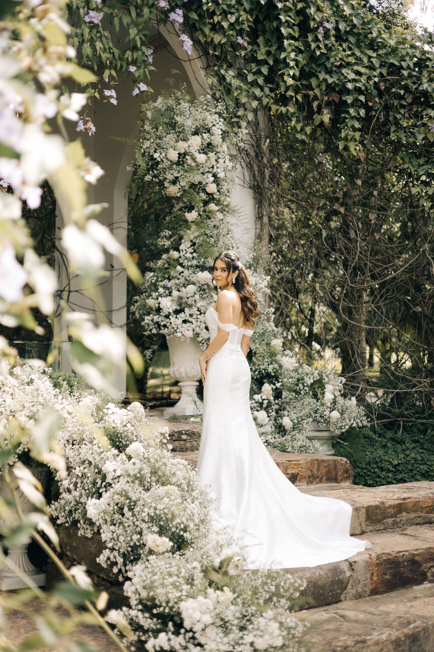 Elegant bridal portrait on stone steps surrounded by cascading white flowers and greenery.