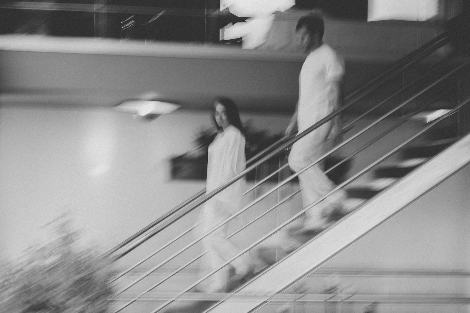 Black and white motion blur photograph of people walking down stairs in an abstract architectural setting.