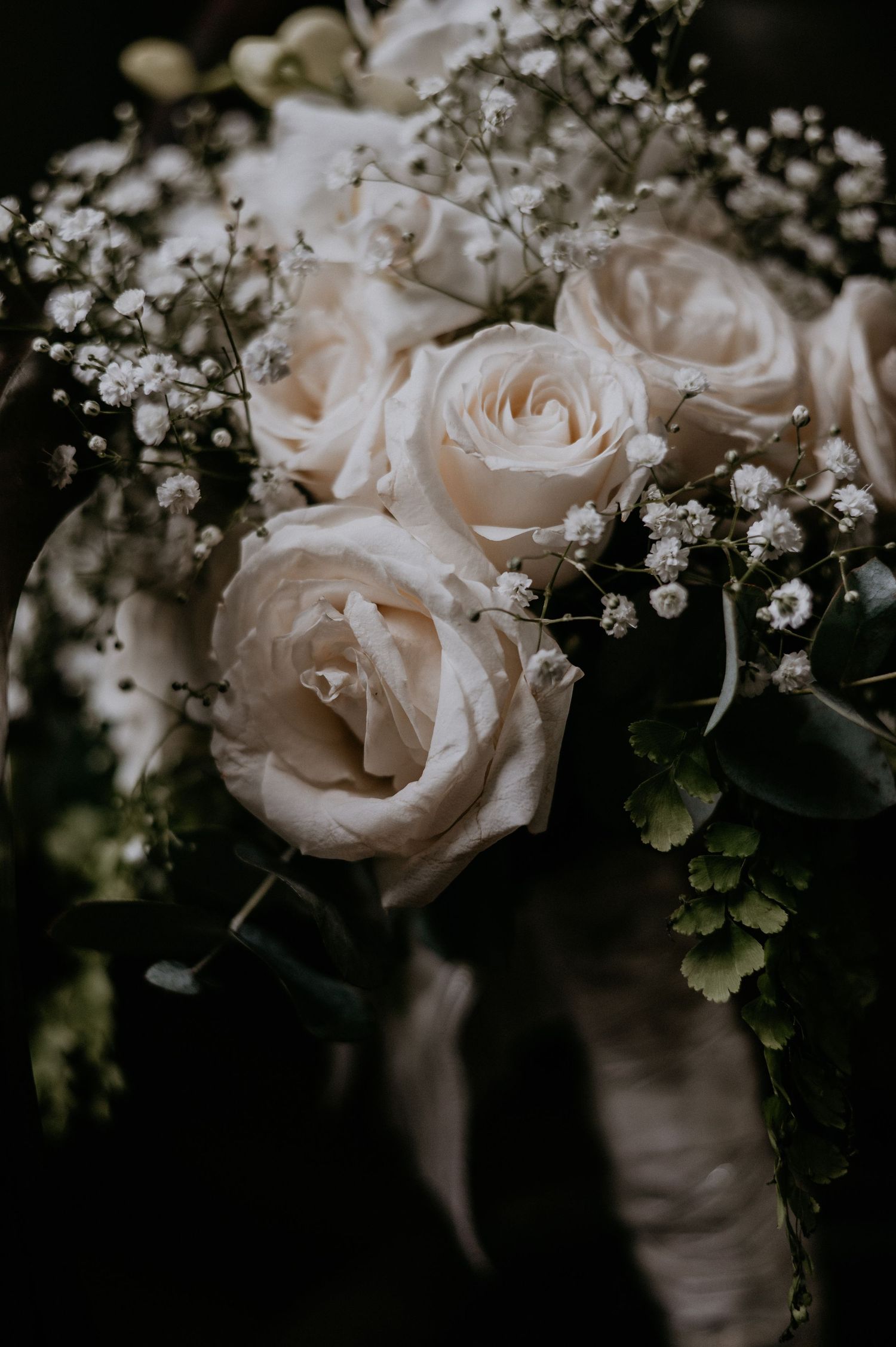 Delicate white roses and baby's breath bouquet photographed in moody lighting.