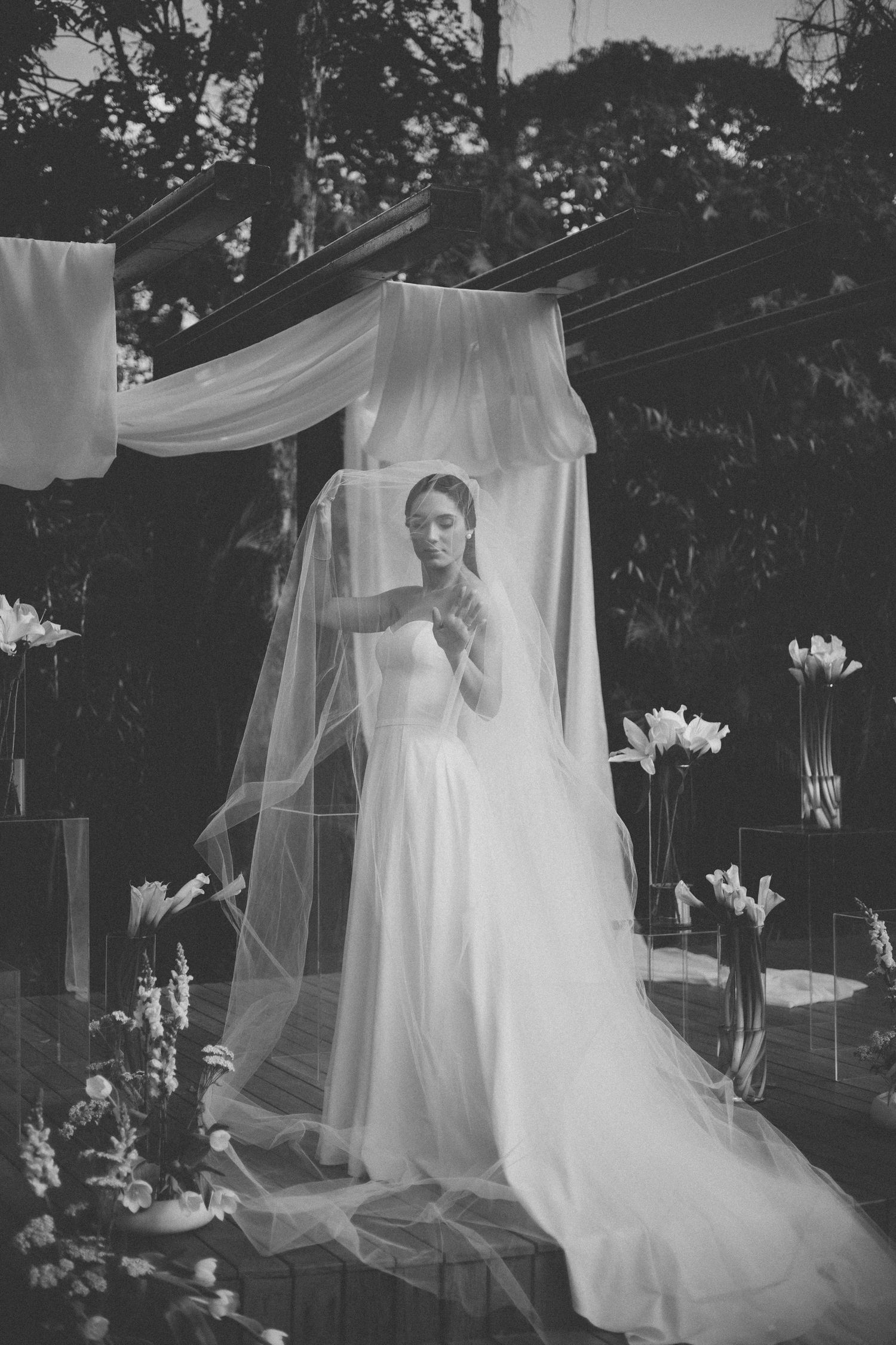 A series of dreamy black and white photos showing a bride behind a flowing veil in an outdoor garden setting.
