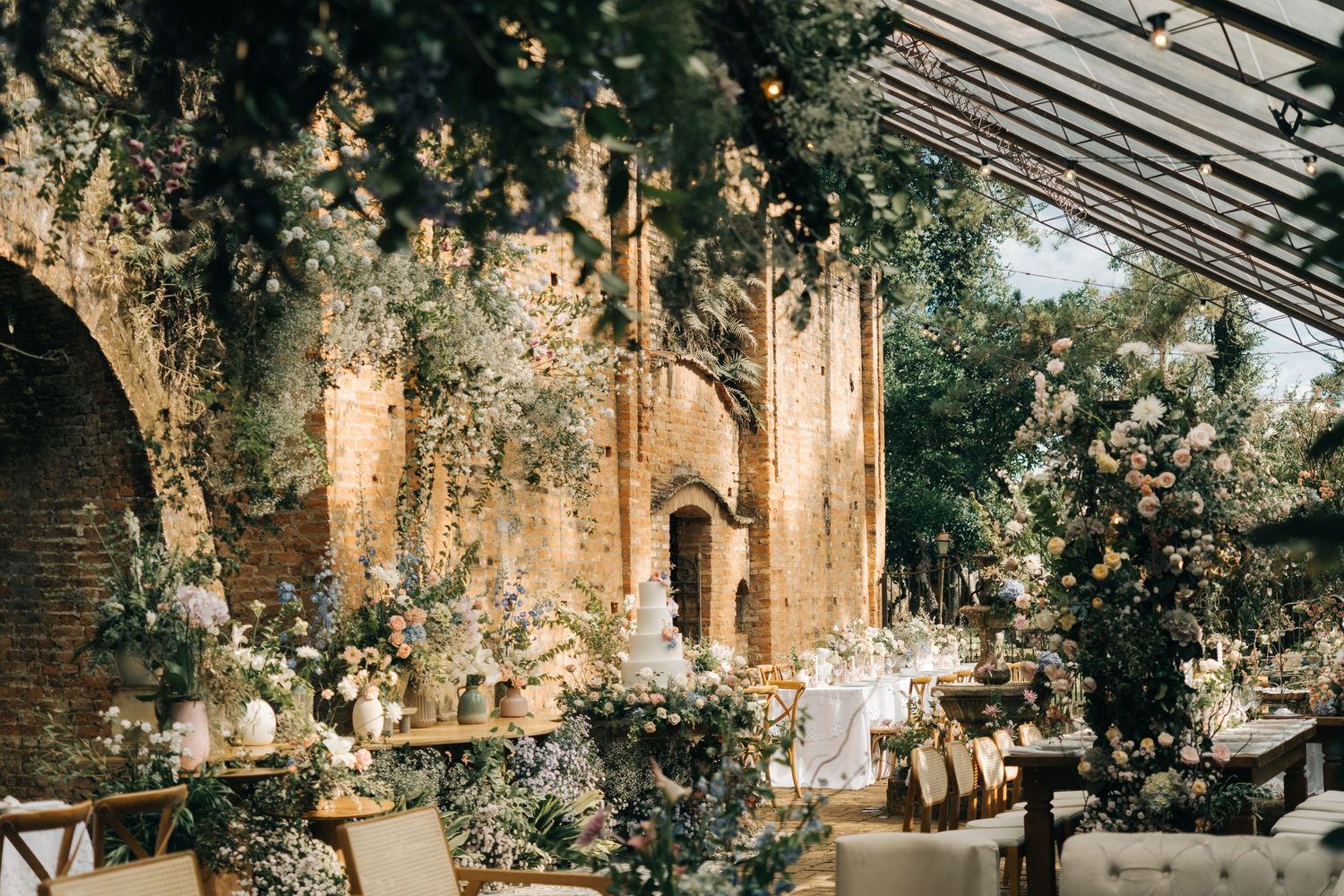 Romantic wedding reception setup in rustic brick venue with climbing roses and glass ceiling.