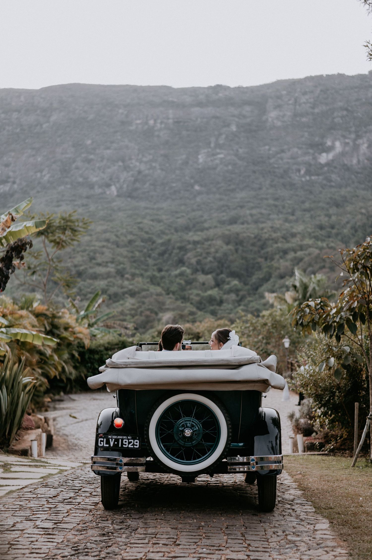 Vintage wedding getaway car parked on stone path with mountains in background.