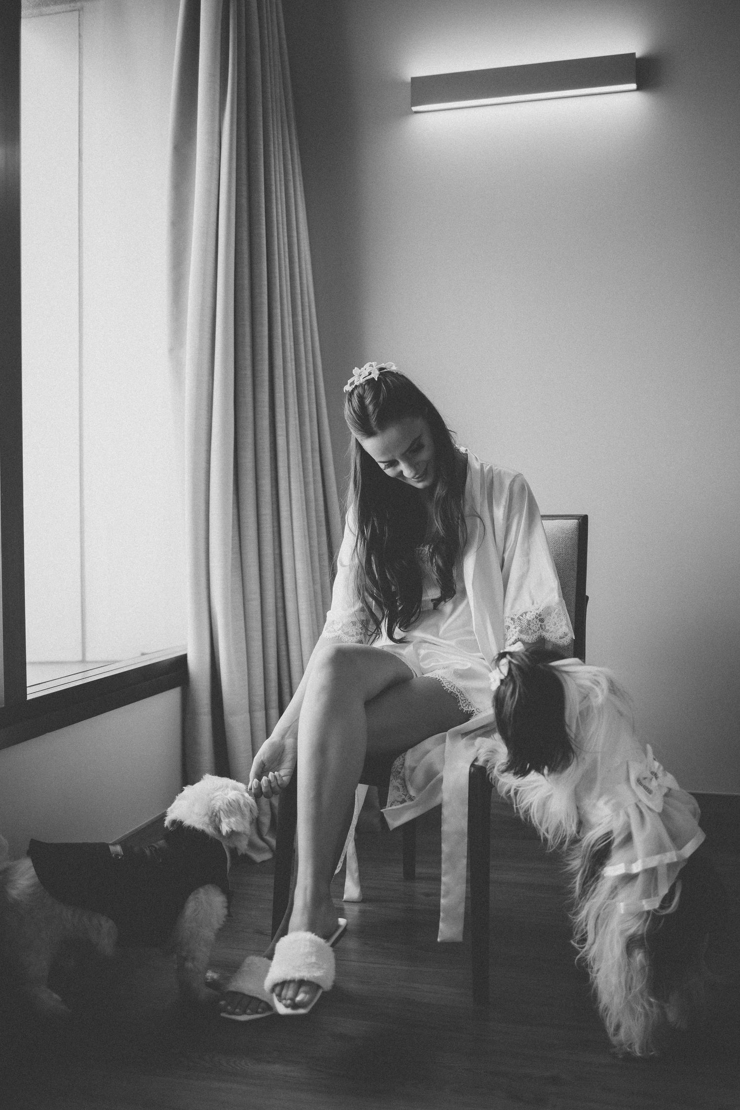 Black and white photo of someone in a white robe sitting with a dog on a hardwood floor.