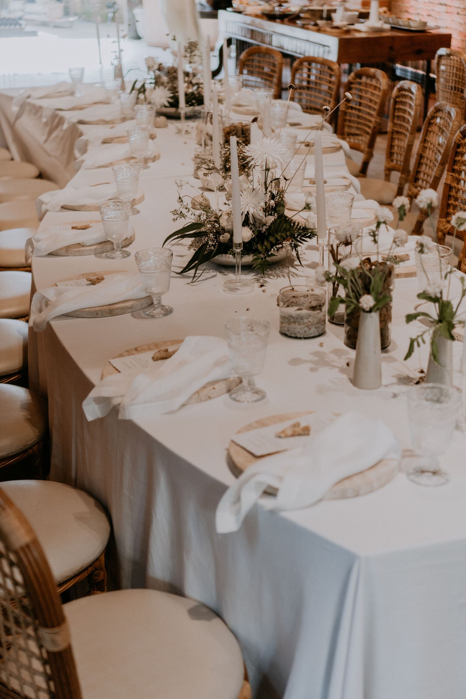 Wedding reception table decorated with white linens, floral centerpieces and rattan chairs.