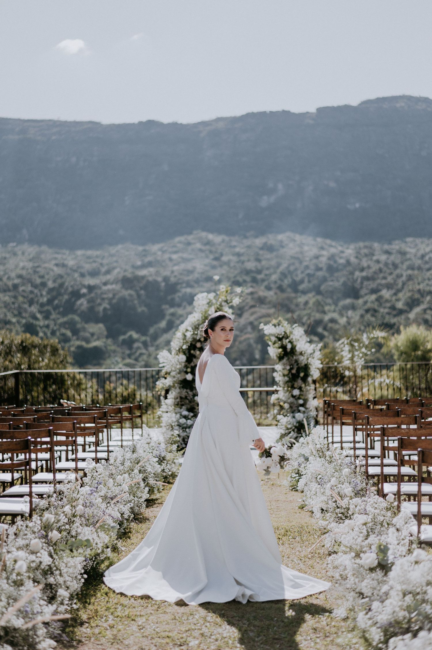 Scenic mountain wedding setup with white floral aisle decorations and wooden chairs.