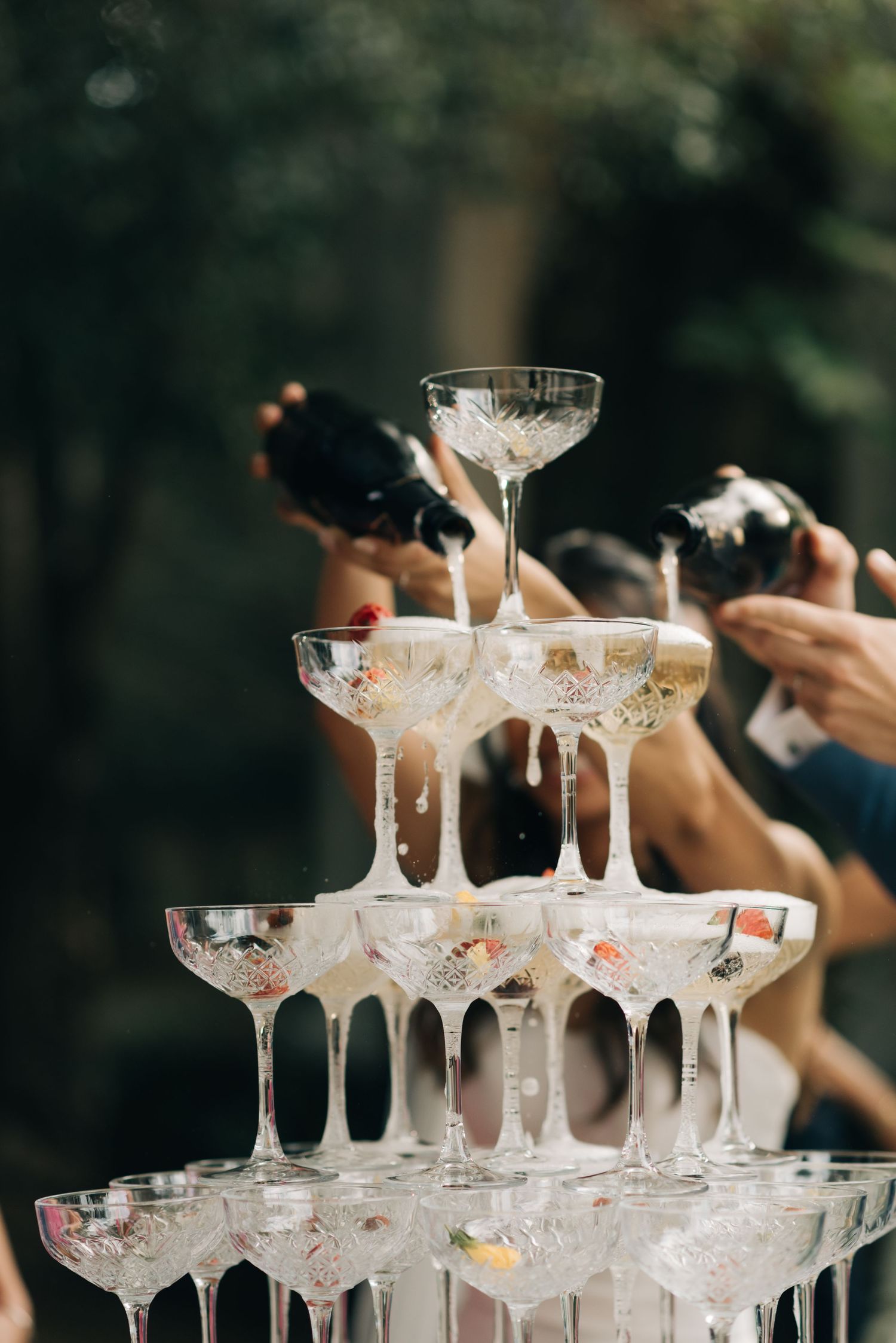 A champagne tower of crystal coupe glasses being filled at an elegant wedding reception.