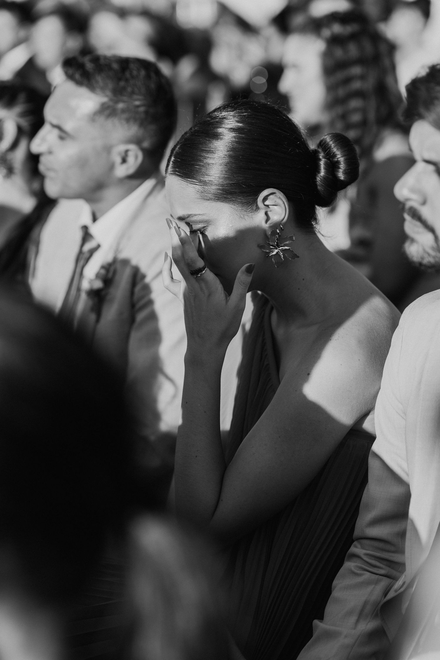 Black and white photo of an emotional wedding guest wiping tears during ceremony.