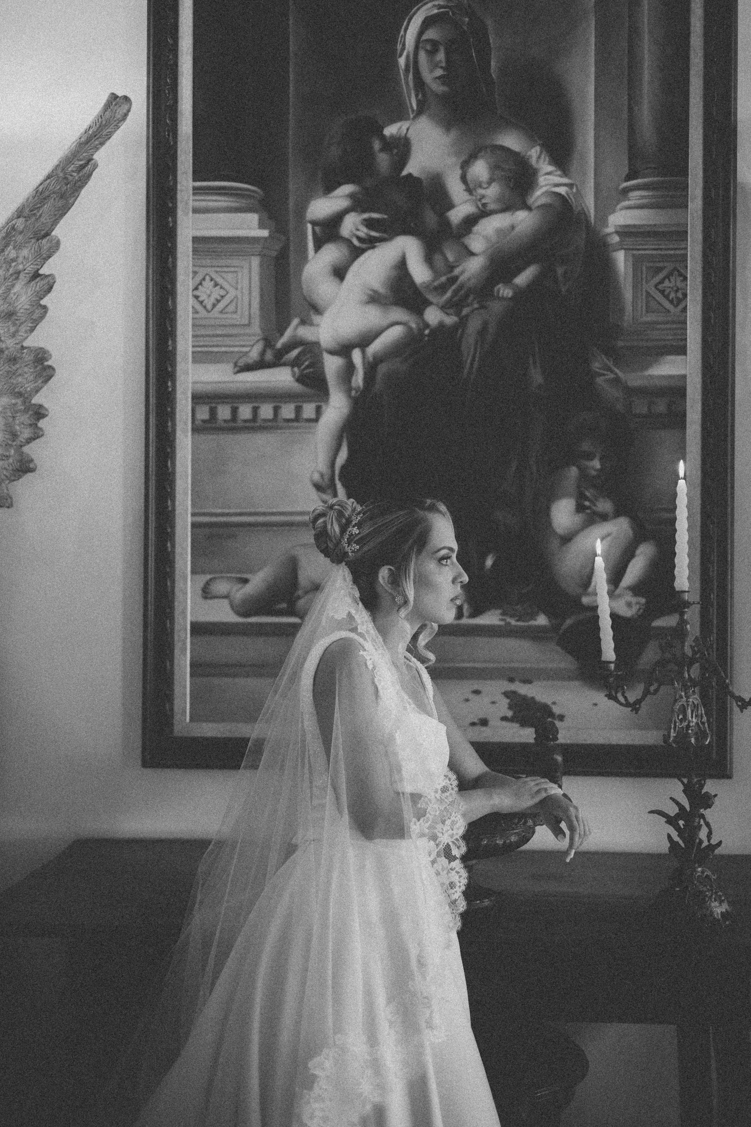 Black and white photo of a bride in front of a classical painting, wearing a long veil and lace wedding dress.