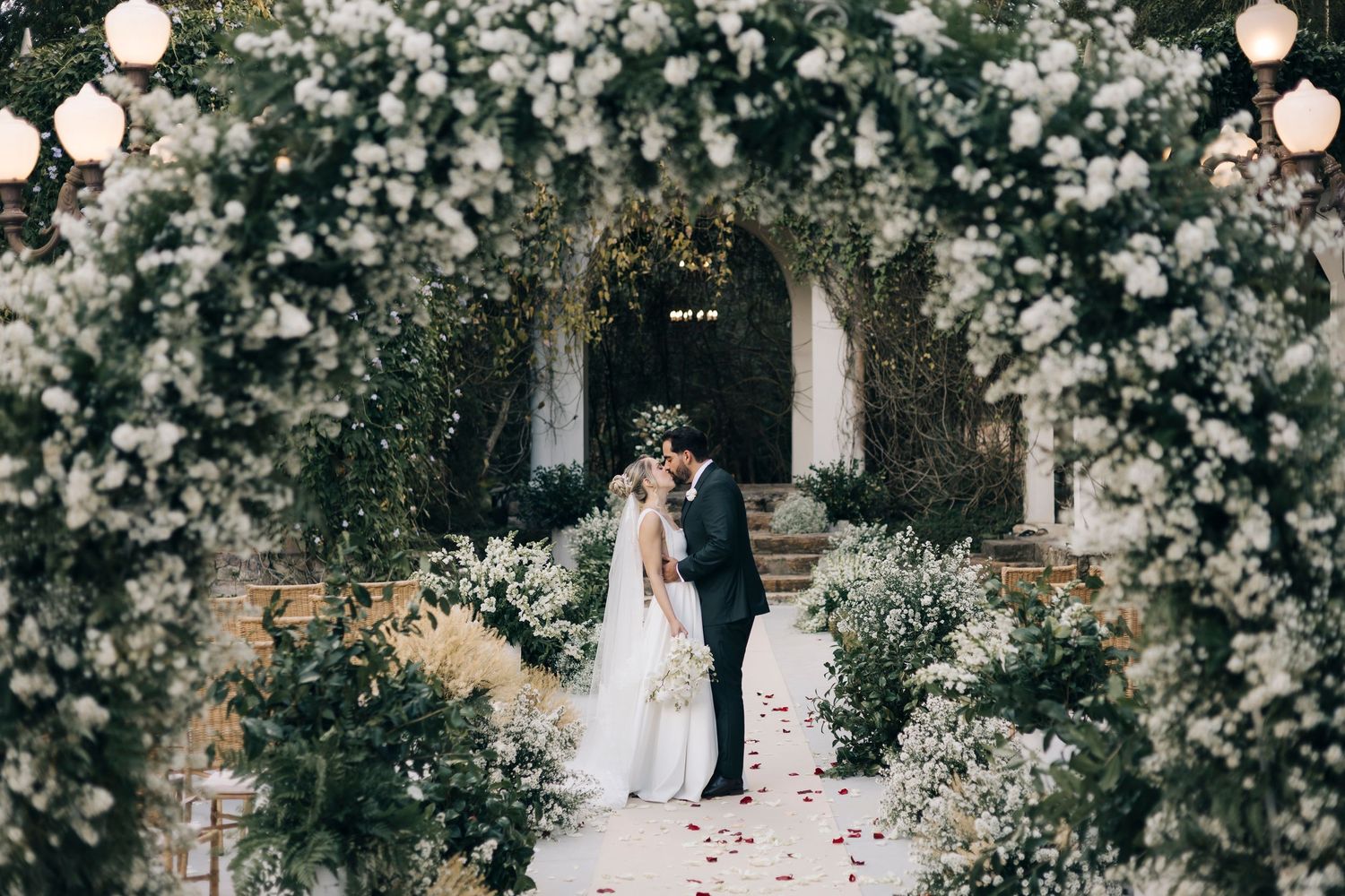 Enchanting wedding arch covered in white roses and greenery with glowing lanterns creating a magical atmosphere.