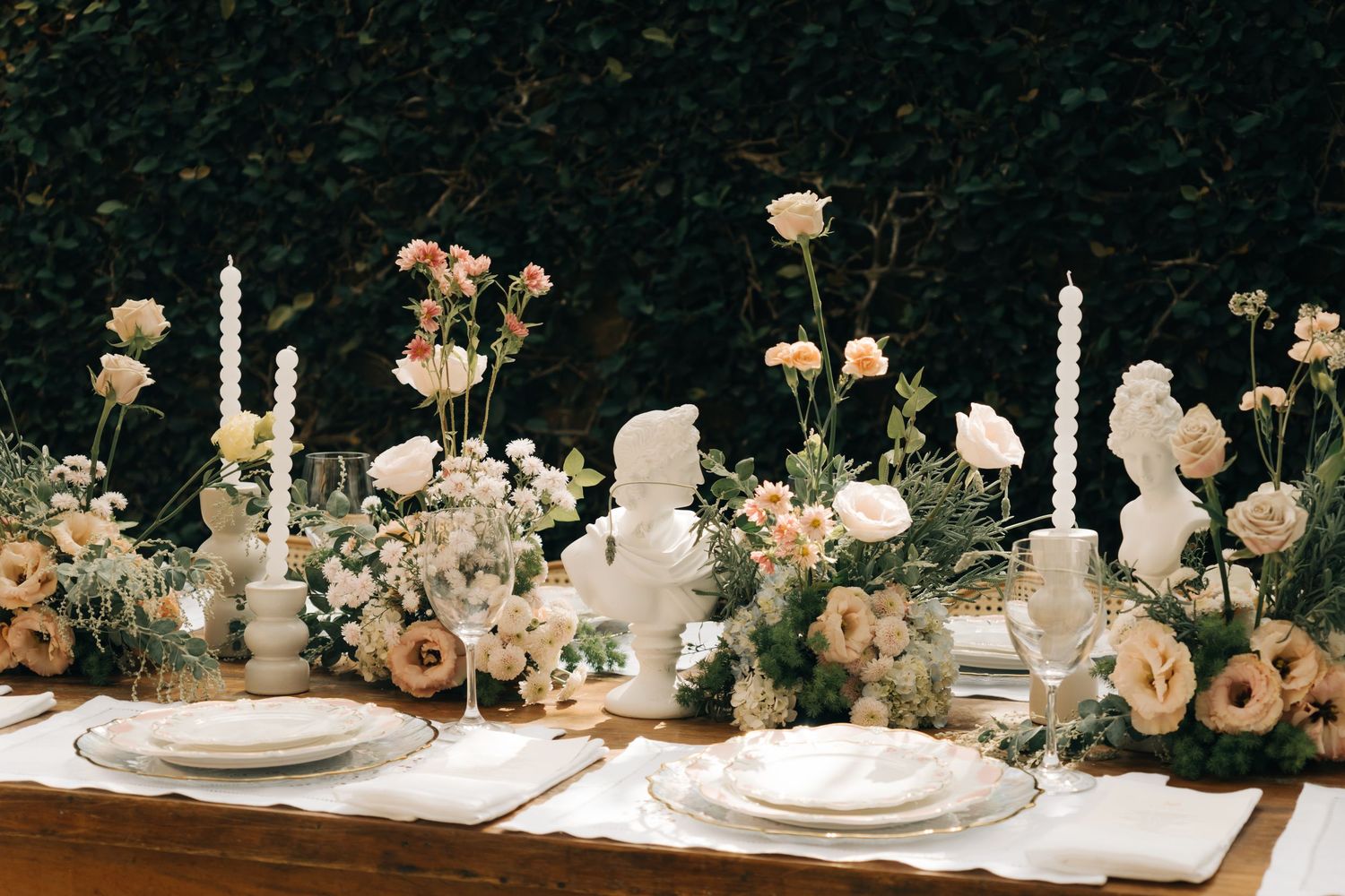 Elegant wedding table setting with white candles, peach roses and vintage decor on rustic wooden surface.