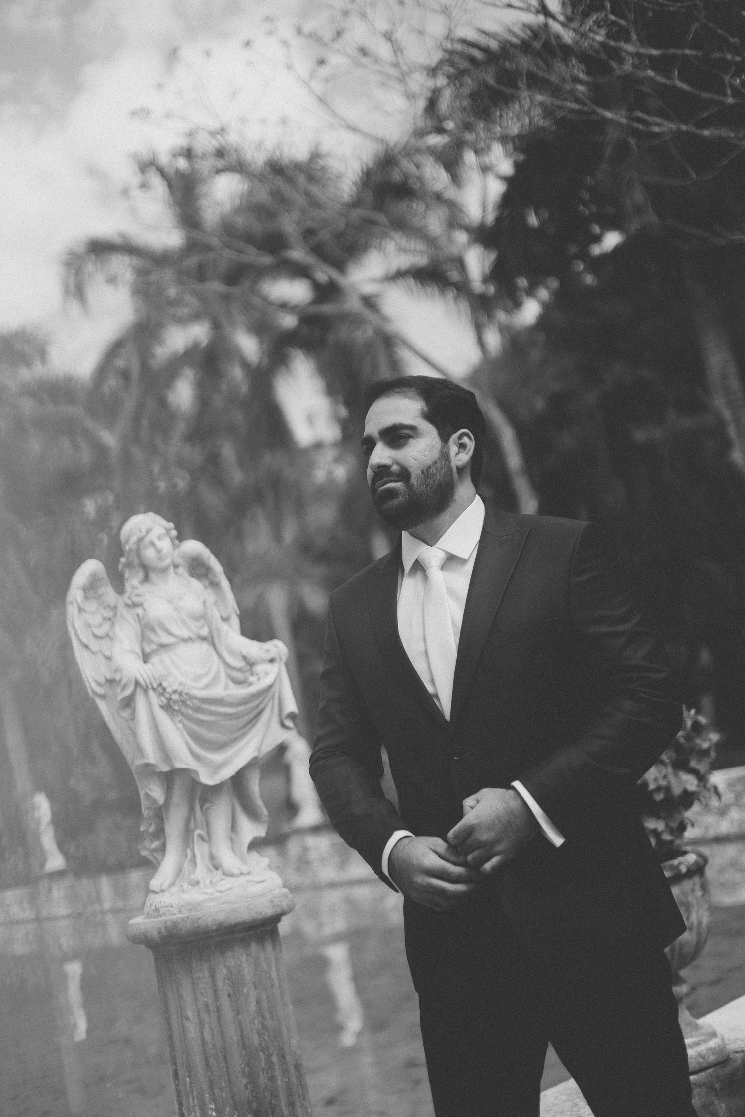 Black and white photograph of a man in a suit standing next to a decorative garden statue of an angel.